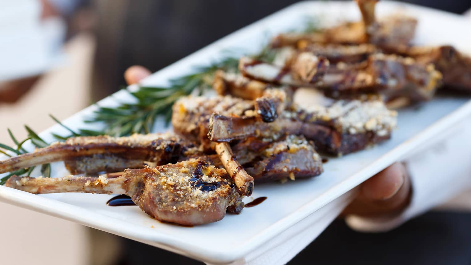 Chef holds white platter with roasted lamb legs