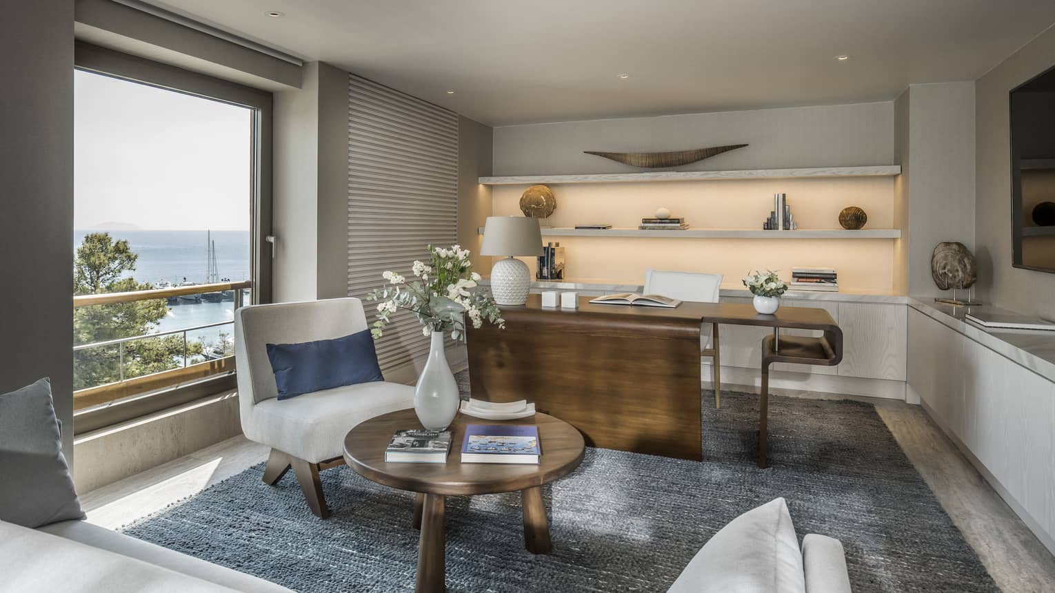 Arion Riviera Suite office with large wooden desk, white accent chair, round coffee table, backlit built-in shelves, ocean views