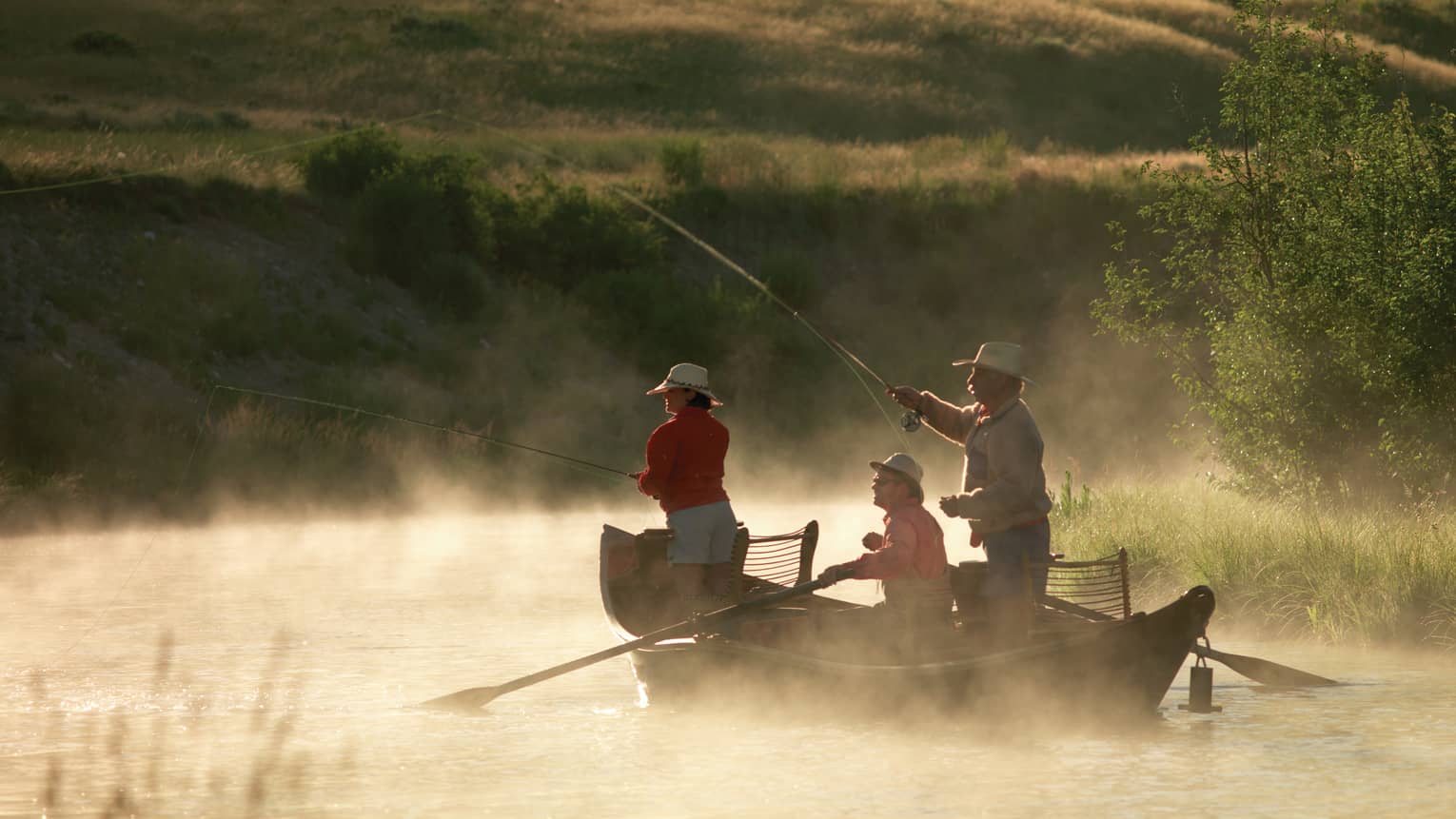 Mist rises from fishing boat on Snake River where three people with hats hold poles, cast lines