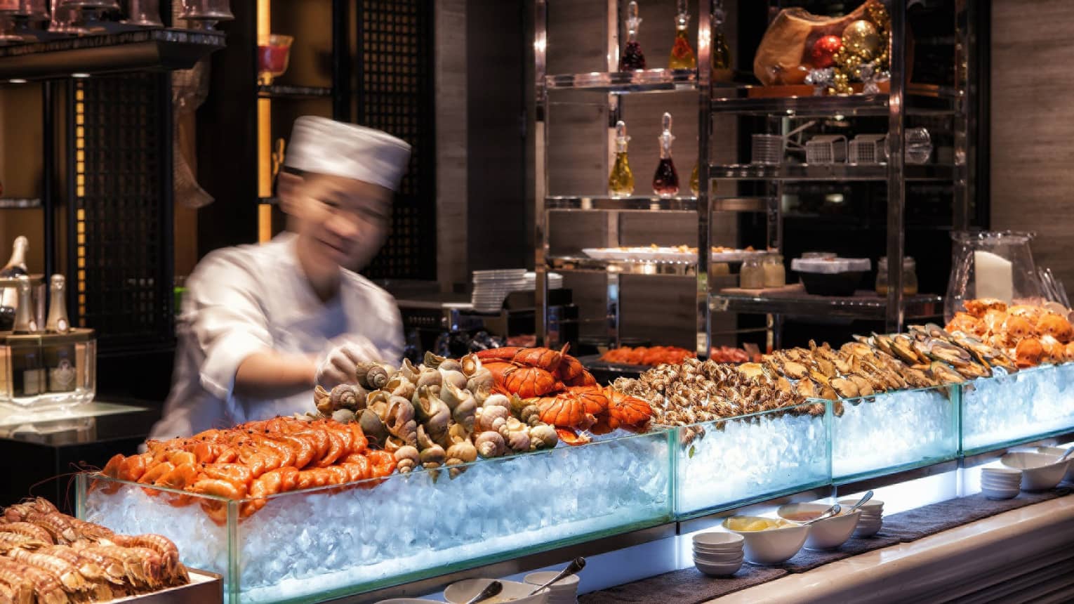 Chef reaches for snails on fresh seafood display on ice at bar 