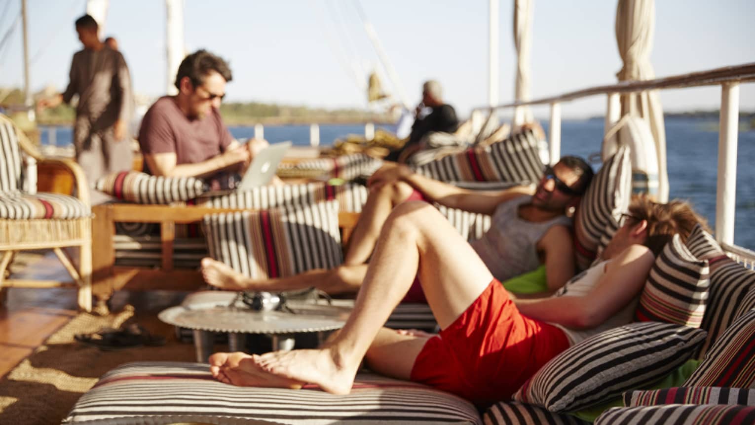 Sunny outdoor patio, people relax on striped lounge cushions