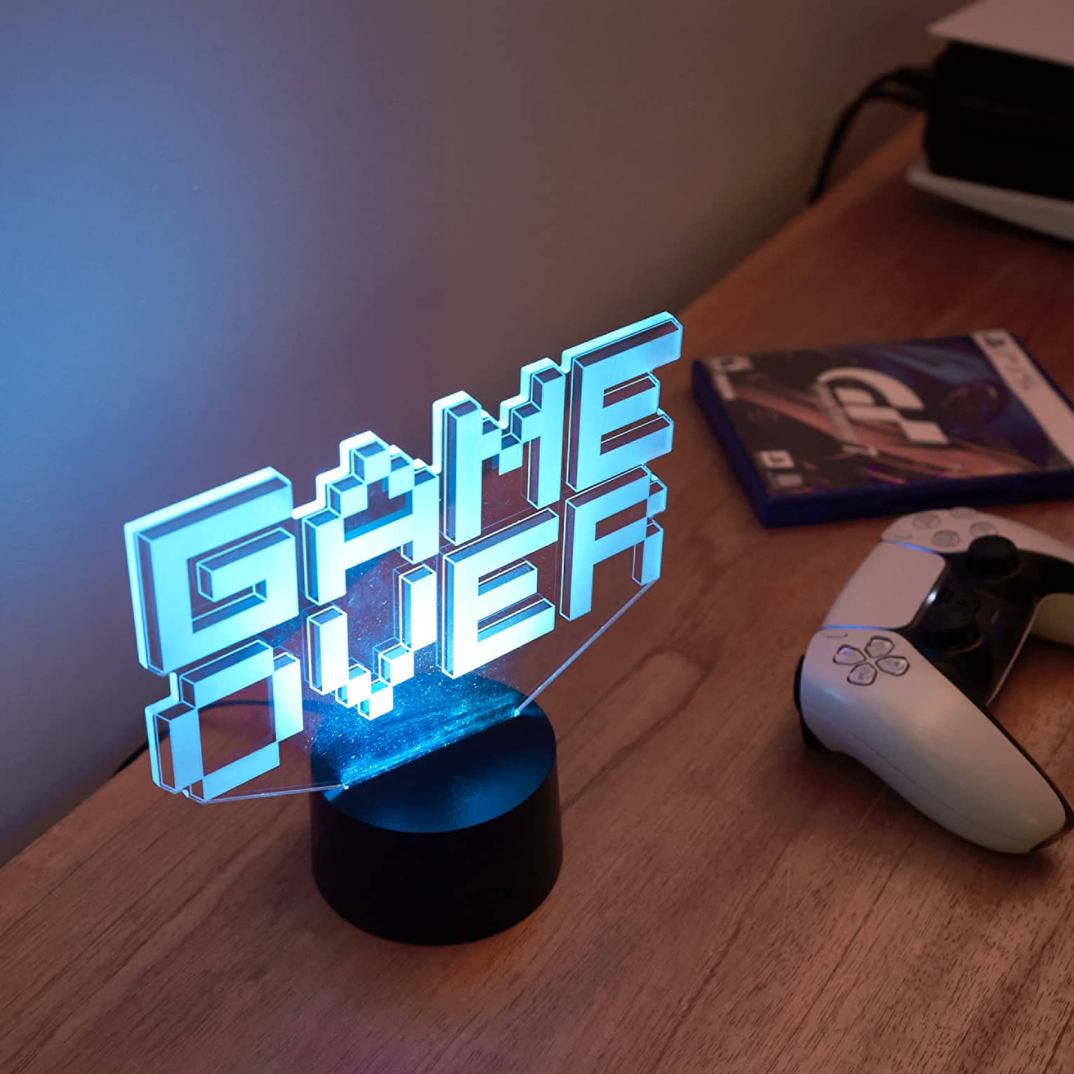 Neon "Game Over" sign in blue letters lights up a wooden table with a white gaming console on it