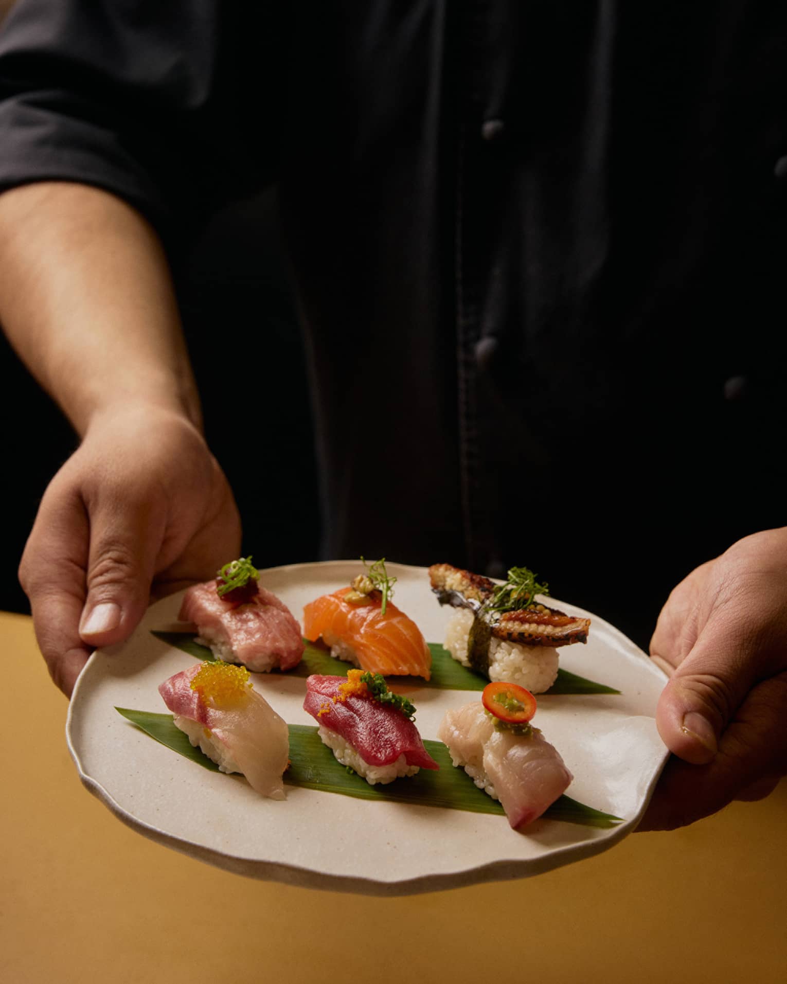 A person in a black shirt holds a plate with six different pieces of sushi.