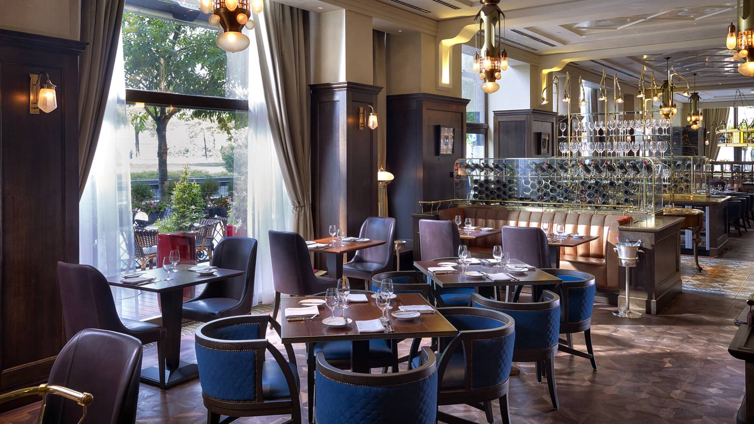 KOLLÁZS Brasserie & Bar dining tables with brown and blue chairs, tall windows, large wine rack