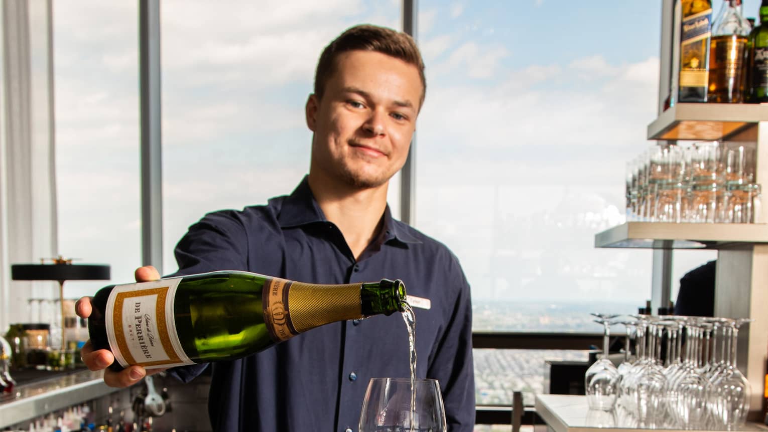 A bartender pours champagne into a cocktail glass