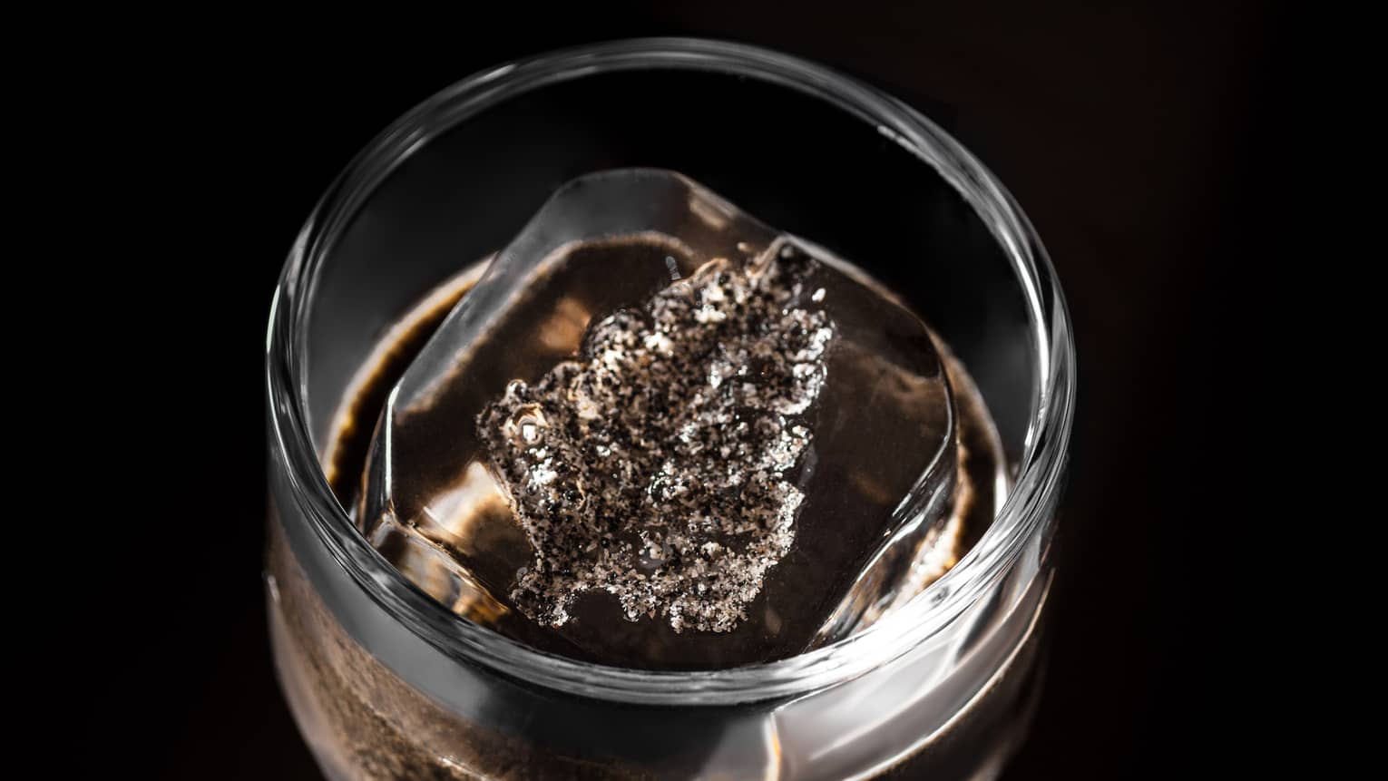 Cocktail in clear glass on dark tabletop with Four Seasons leaf?shaped ice cube