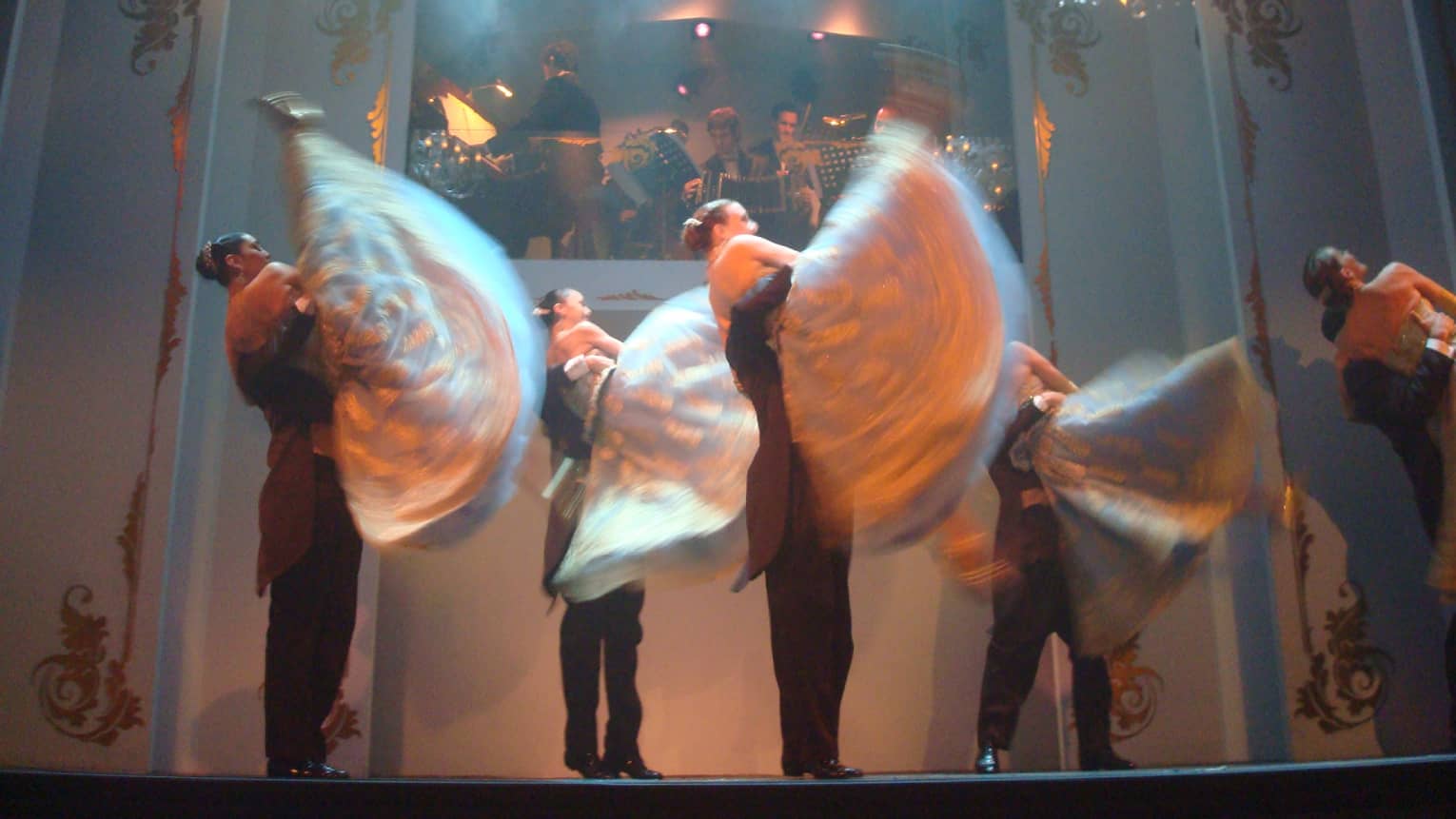 Tango dancers twirl on stage under small chandeliers, lights 