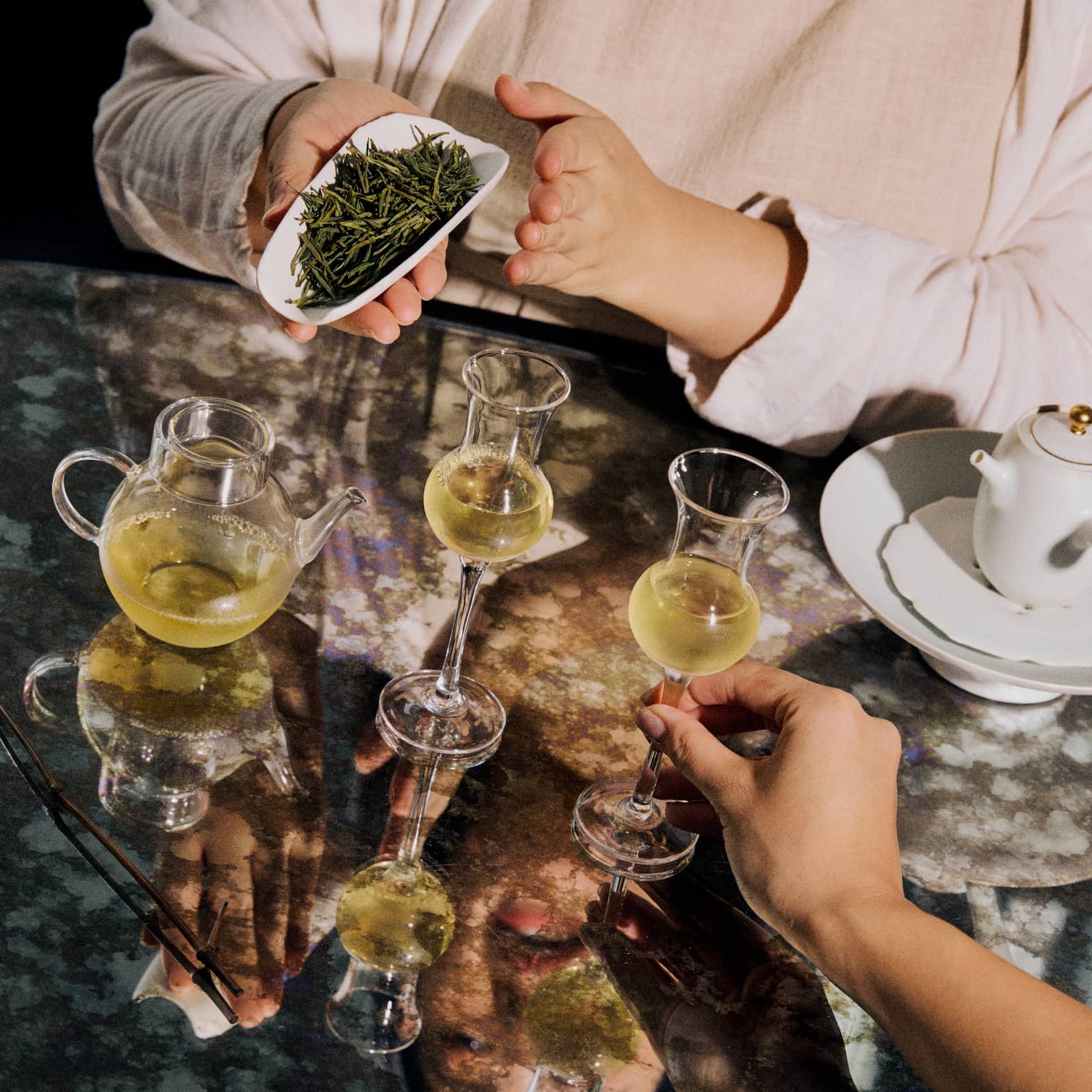 Loose leaf green tea displayed alongside two clear glasses of tea and a teapot.