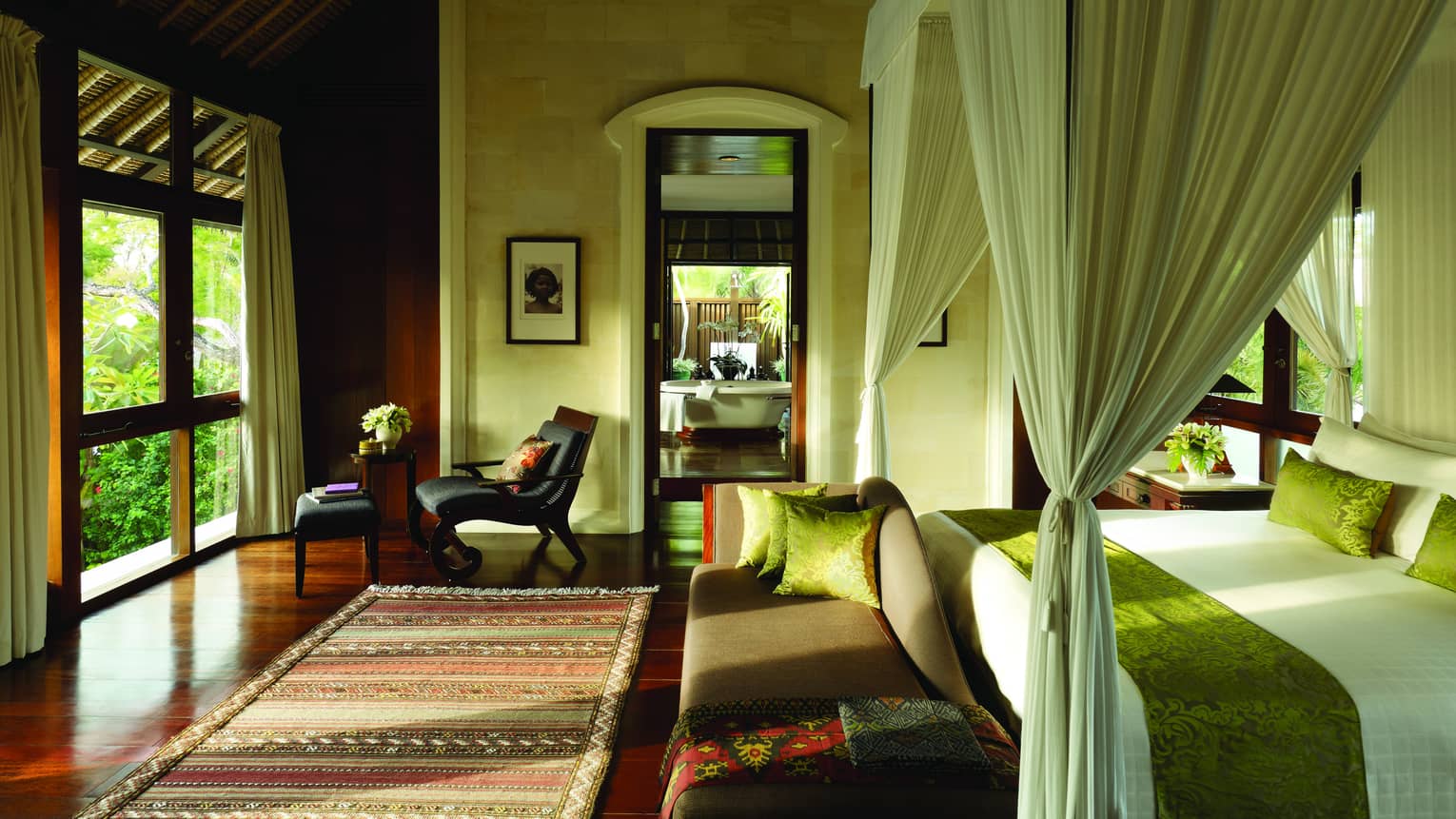 Sunlight coming in bedroom over Balinese rug, small chaise at foot of bed with velvet green sash, white curtains