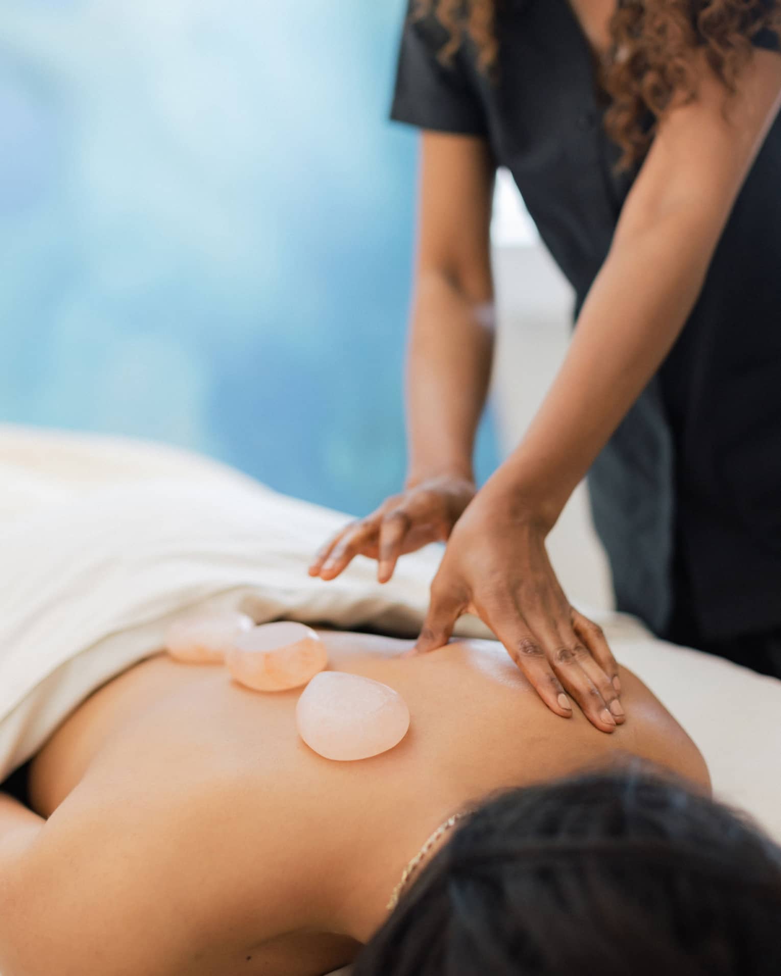 Masseuse places salt stones on a person's bare back