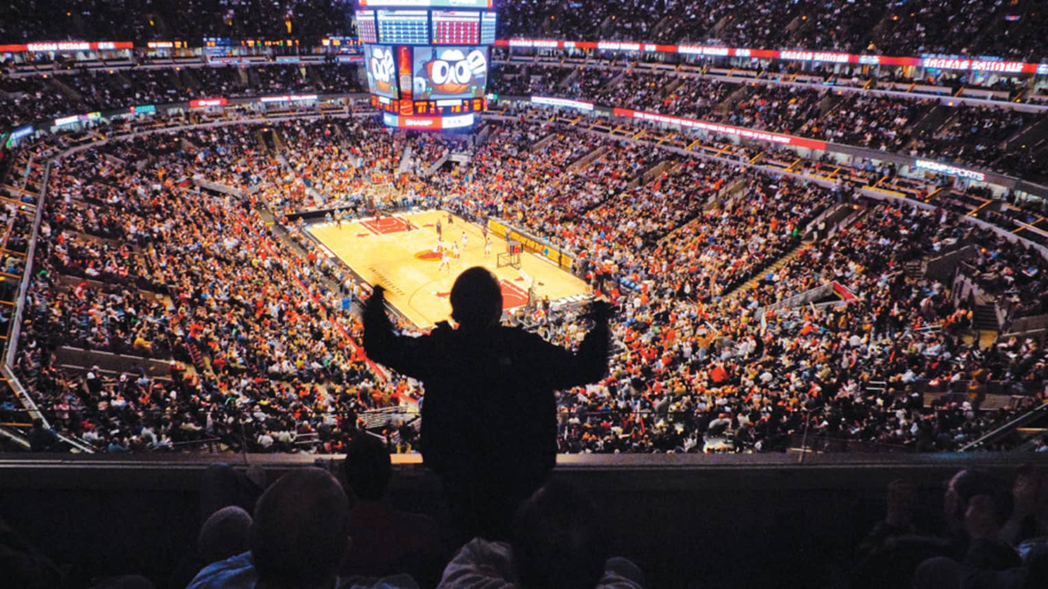 A man cheering in a crowd at a basketball game in a large stadium.