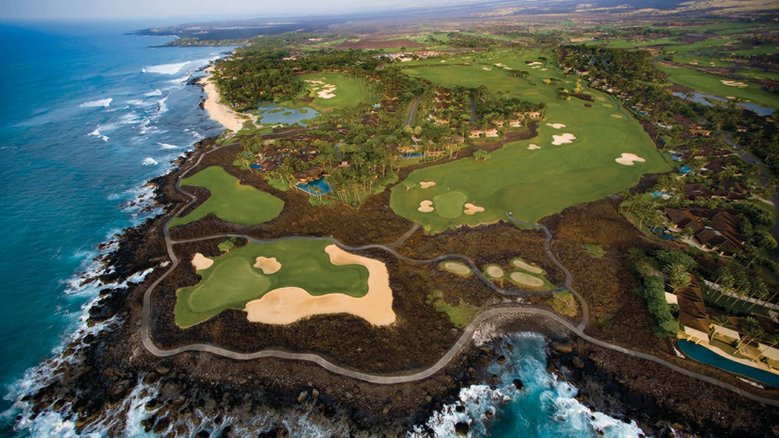 Aerial view of 18-hole golf course greens on volcanic rock by ocean