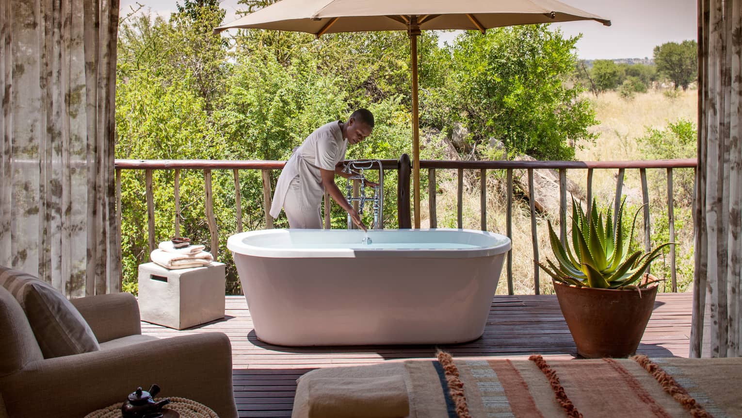 Woman draws bath in freestanding tub on patio beside large cactus plant in pot