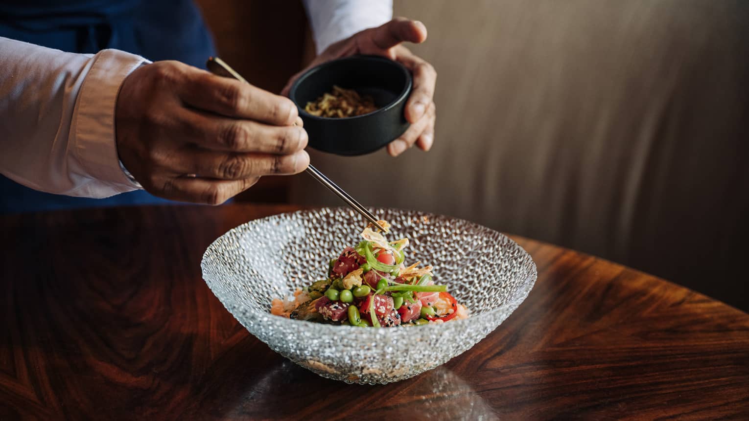 Waiter uses chopsticks to place item on top of salad in a clear glass bowl