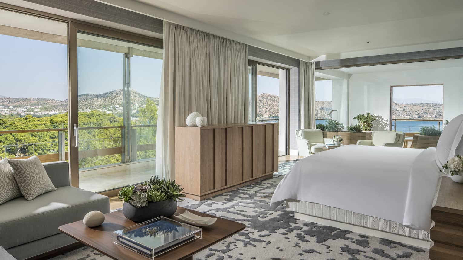 Arion Riviera Suite with white King bed, blonde wood sideboard, grey sectional sofa with square coffee table, panoramic ocean views