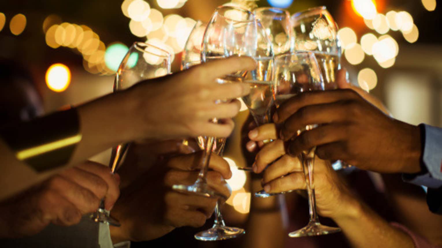 A group of guests clink their glasses of champagne together on a patio with twinkle lights