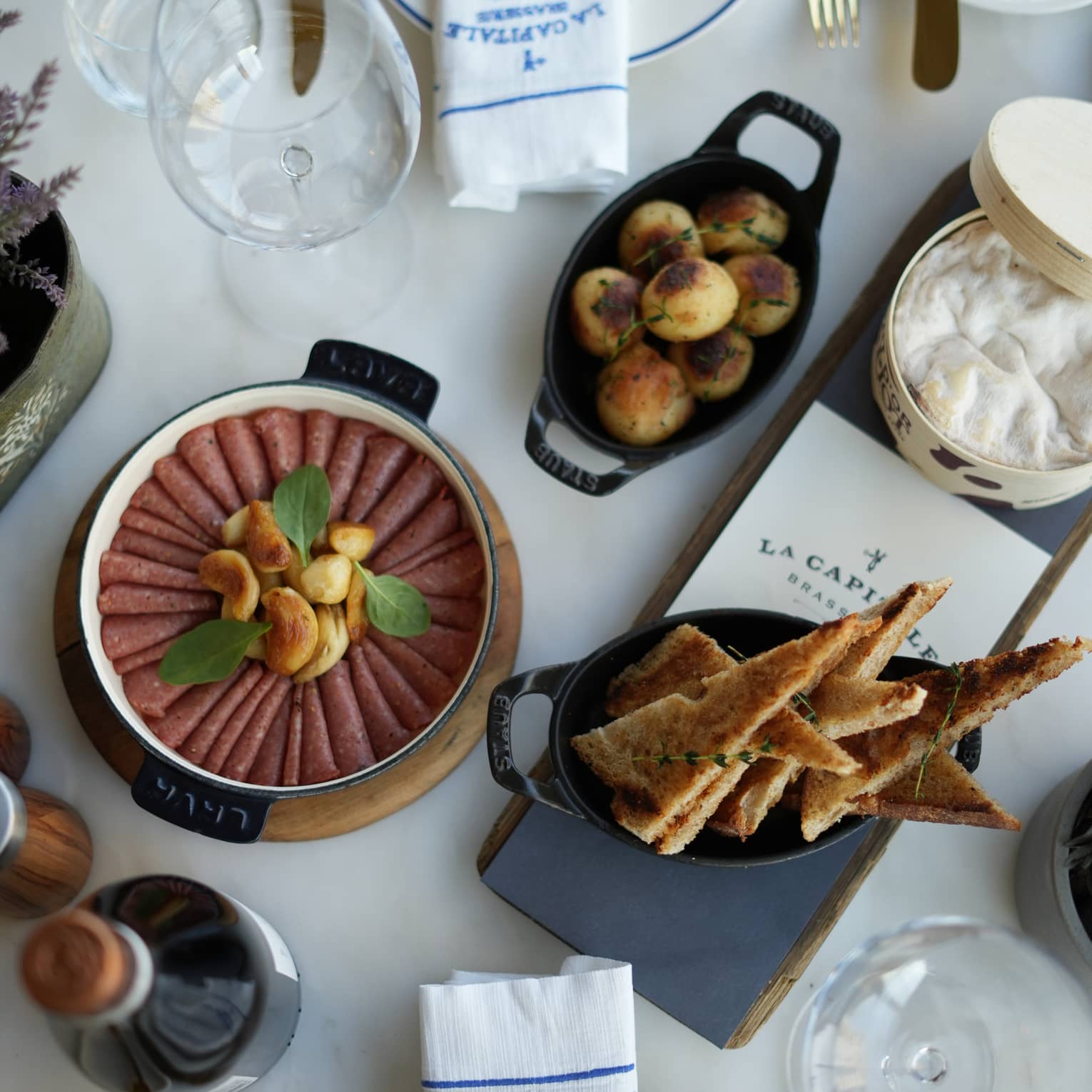 Sliced meat, small roasted potatoes and triangle crisps served next to a container of Mont d'Or cheese