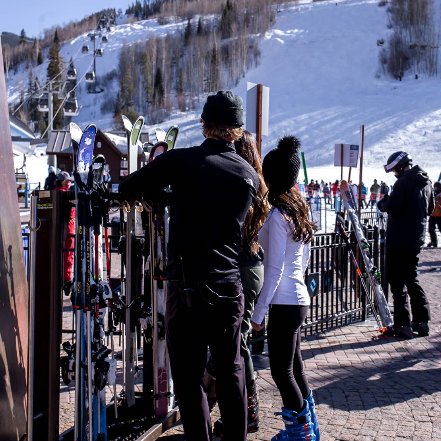 A group of people looking at skis and snowboards outside near a hill with snow on it.