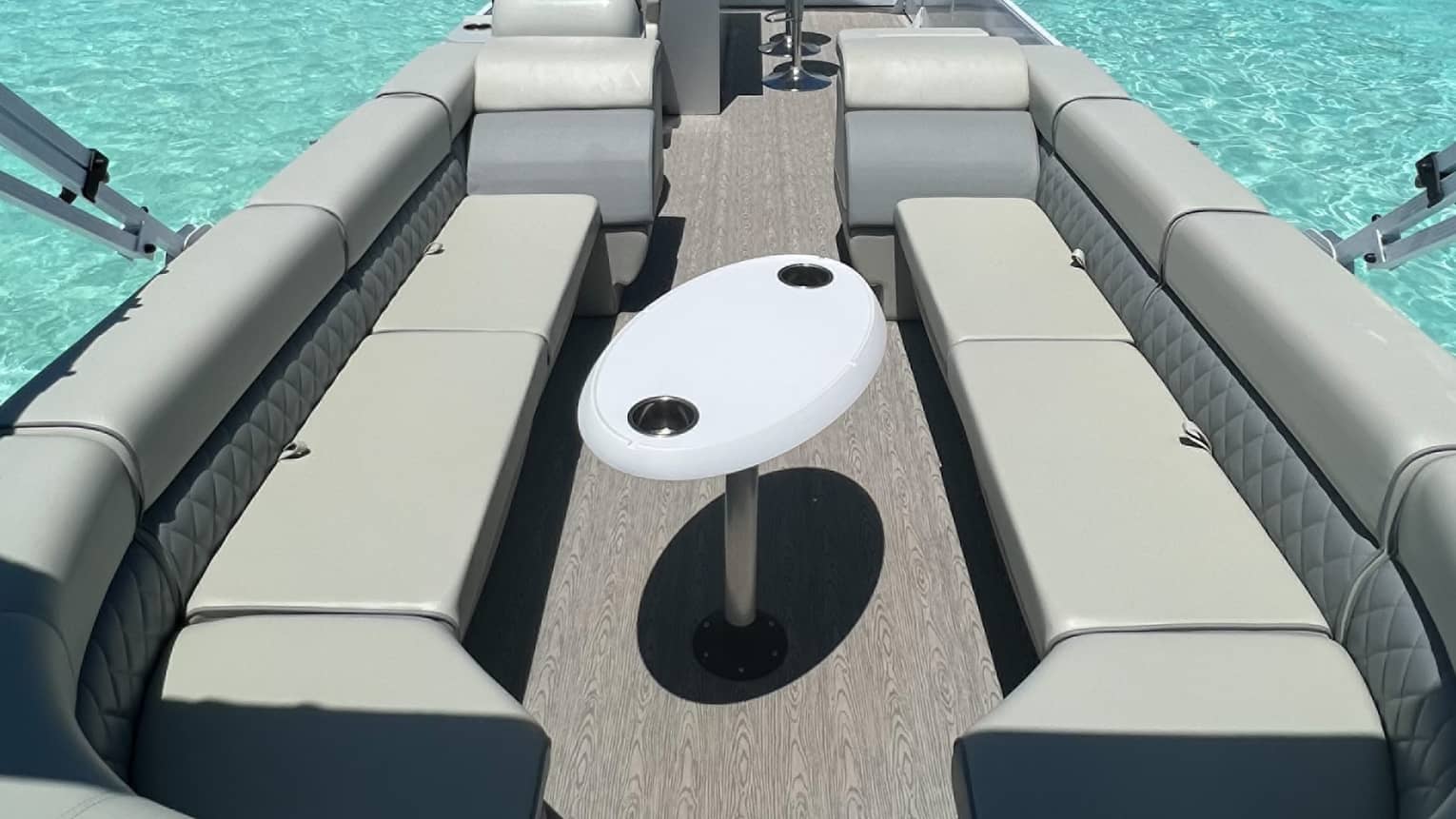 Interior view of a speedboat furnished with padded benches and a small table, the turquoise ocean visible on either side.