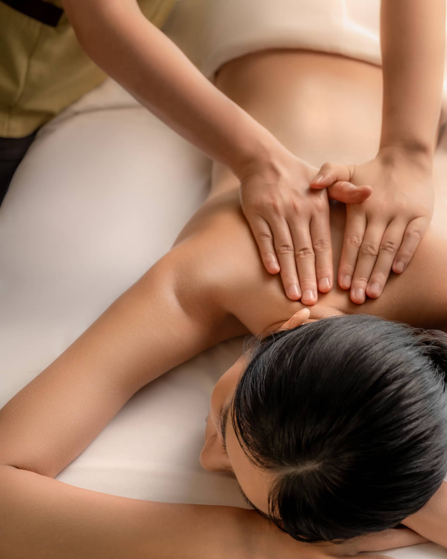 Two hands apply gentle pressure on the bare upper spine of a guest lying on their stomach on a massage table.