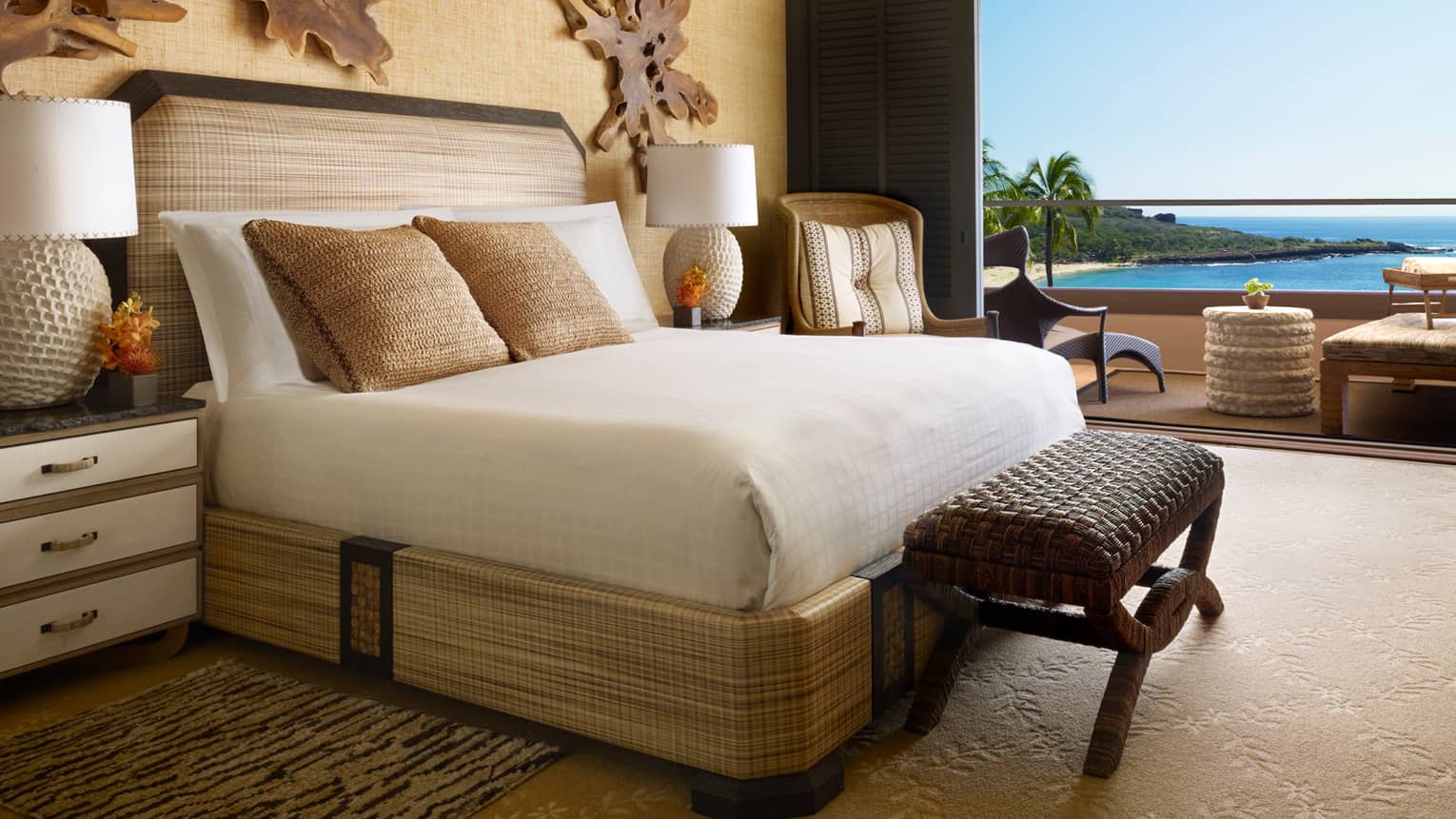 Palawai Suite bed with wicker frame, bench, burlap pillows, rustic driftwood art on walls, open wall to patio