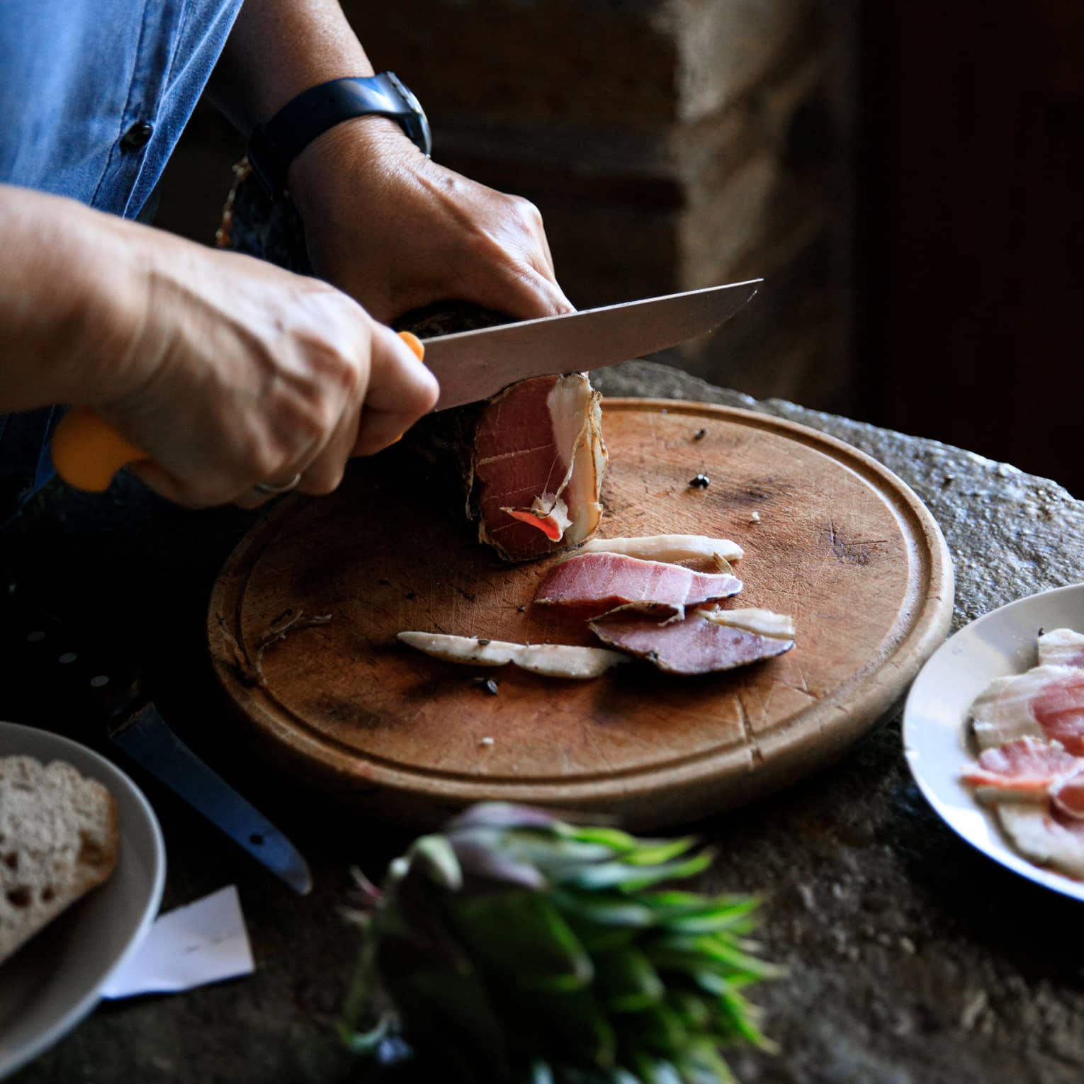 Person cutting Louza (Aegean prosciutto) on round cutting board