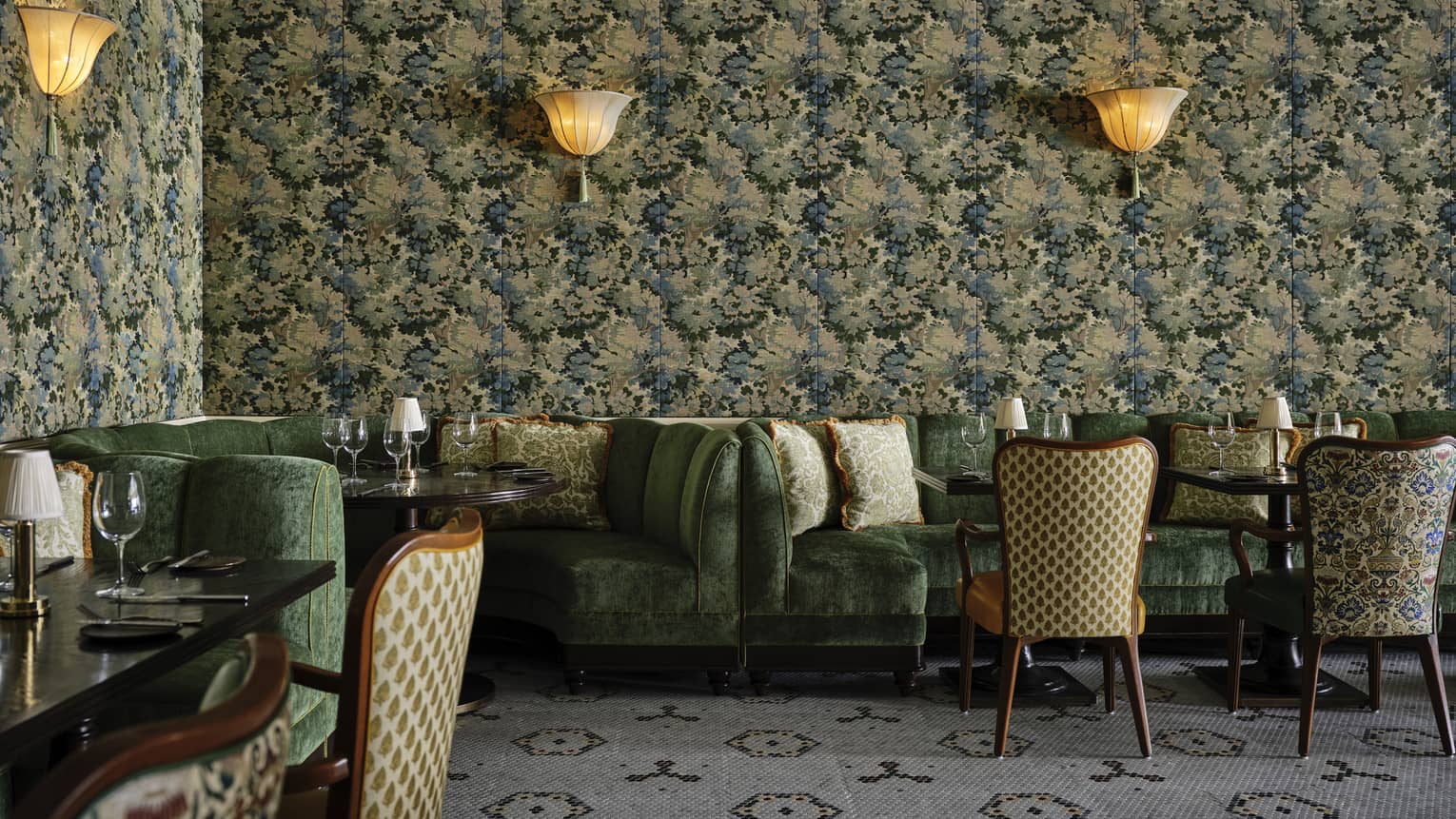 The corner of a dining outlet with colourful green wallpaper, green booths and chairs and sconces.