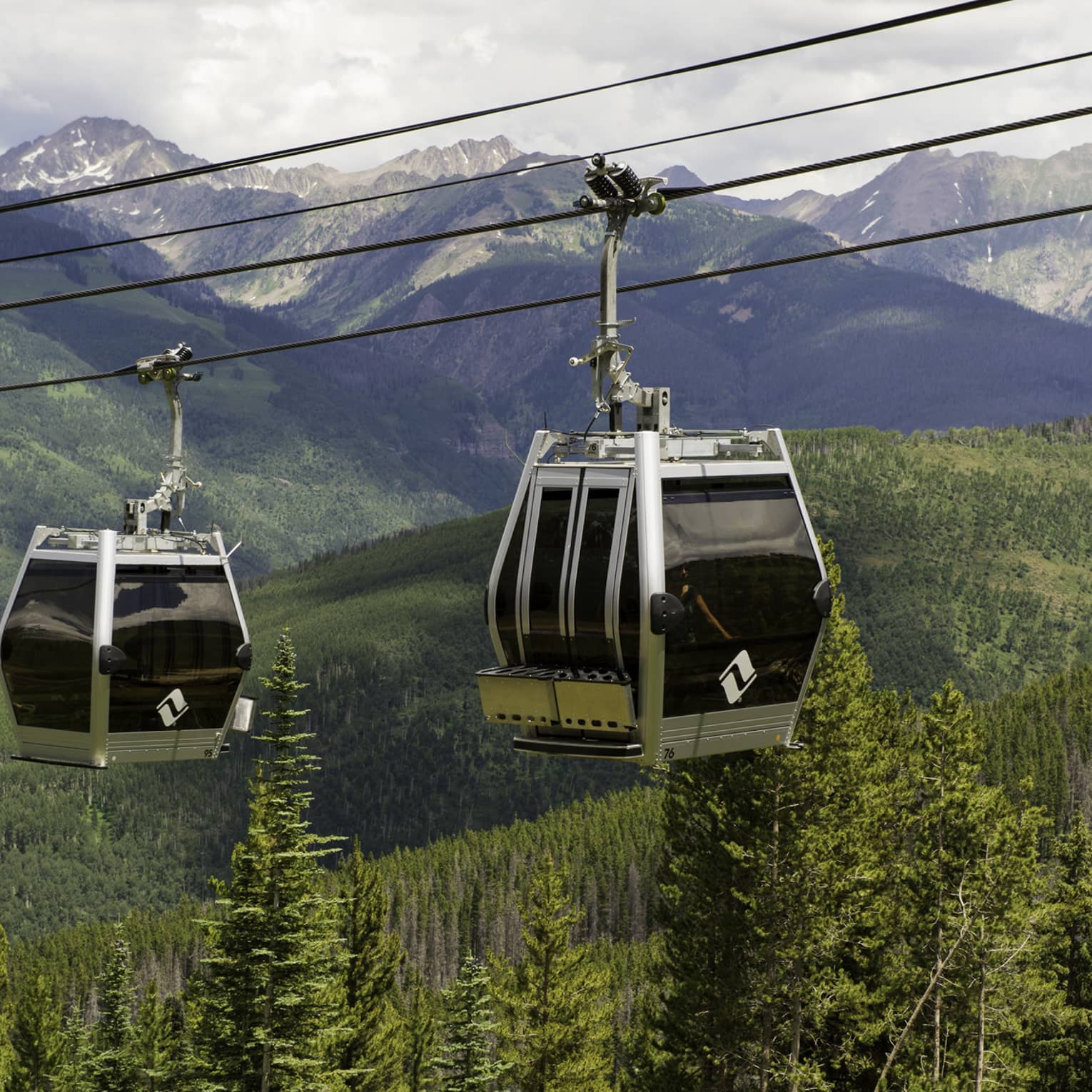 Two gondolas travelling over a forested area.