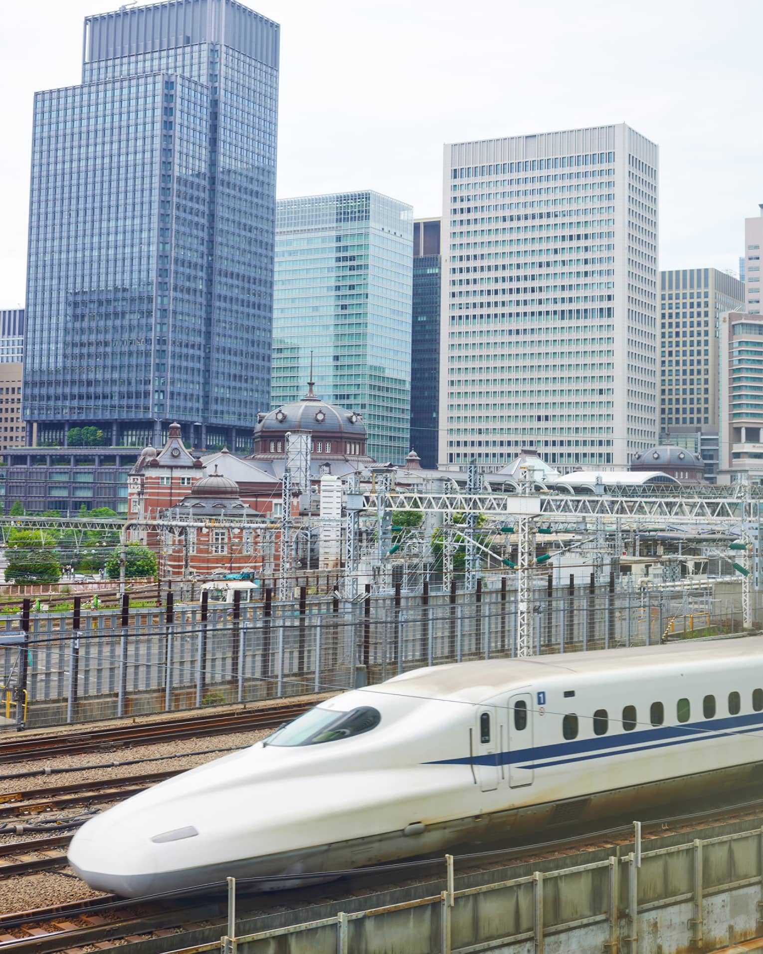 The Shinkansen bullet train speeds past Tokyo's railway station dwarfed by the skyline of rectangular, glass high-rises.