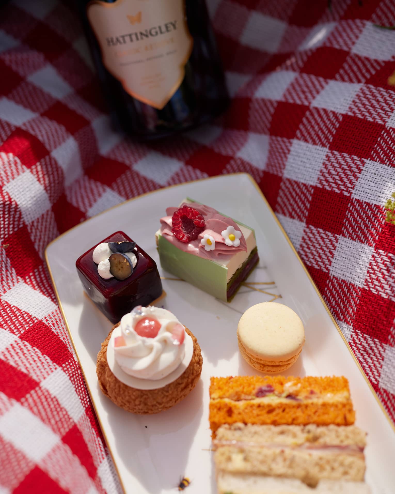 Desserts on a plate placed on a picnic blanket and a bottle of wine beside it