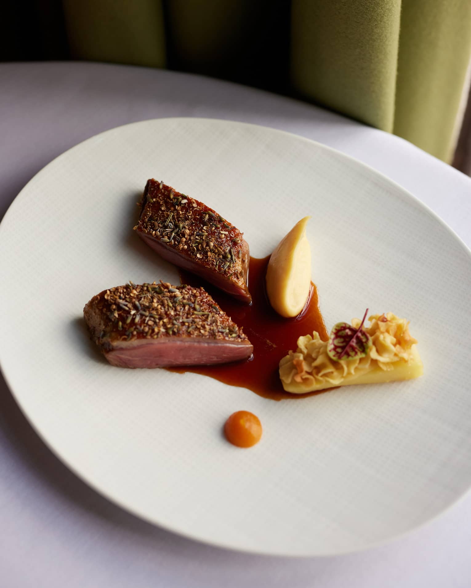 A round white plate holds food items with garnishes and a sauce.