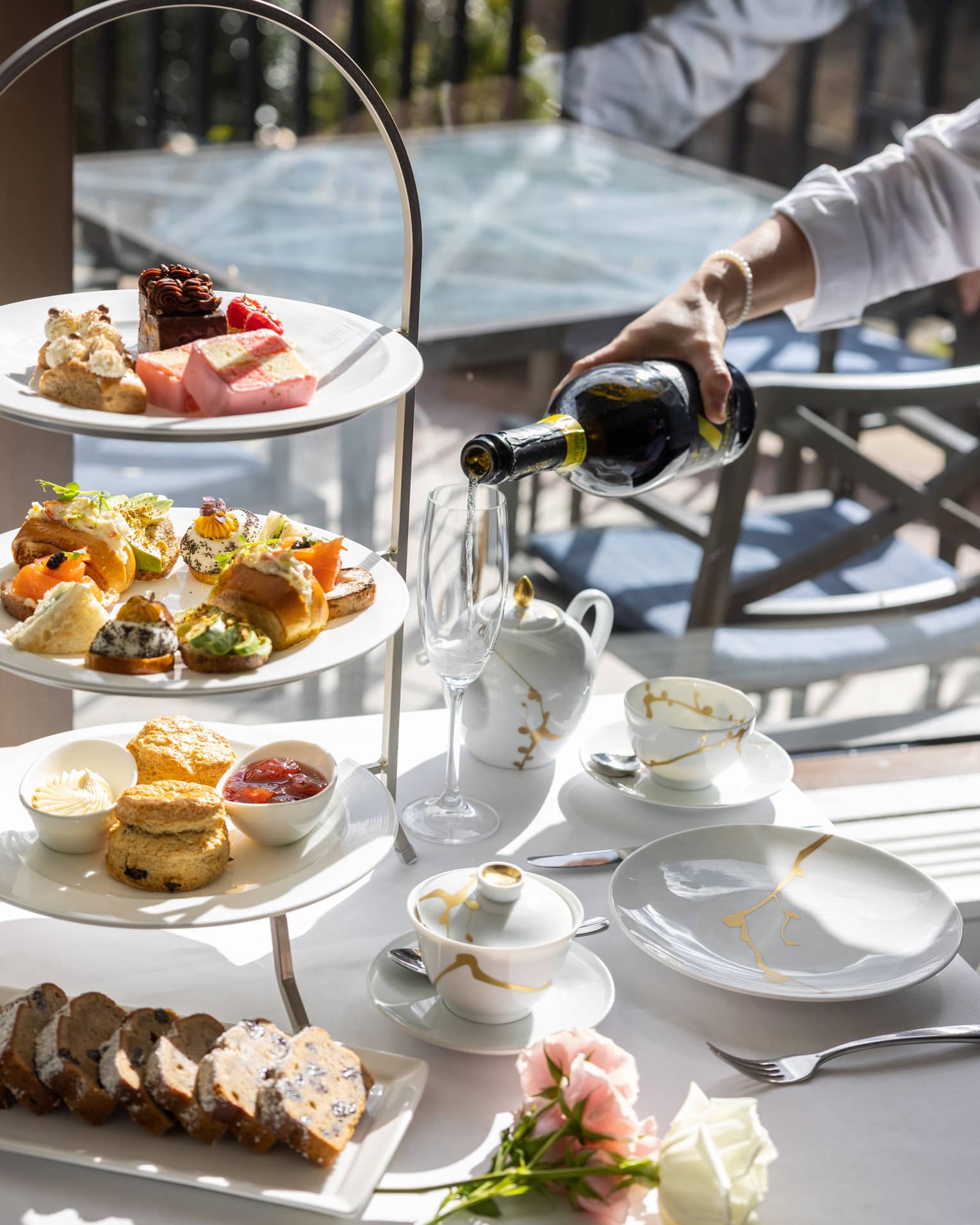 Champagne being poured next to a tiered assortment of afternoon tea small foods and pastries.