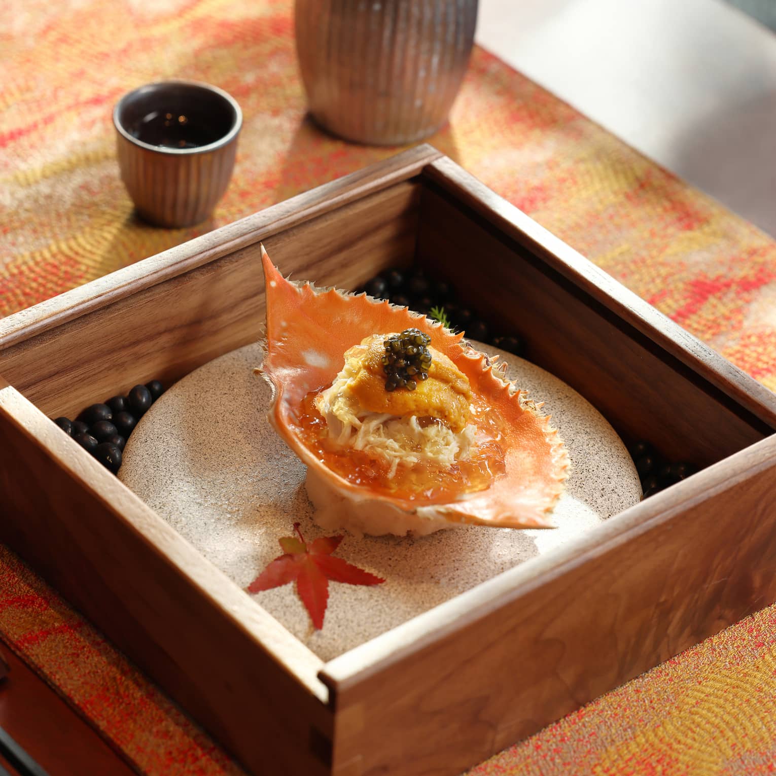 Bottle of sake and crab dish with decorative autumn leaves at elegant restaurant