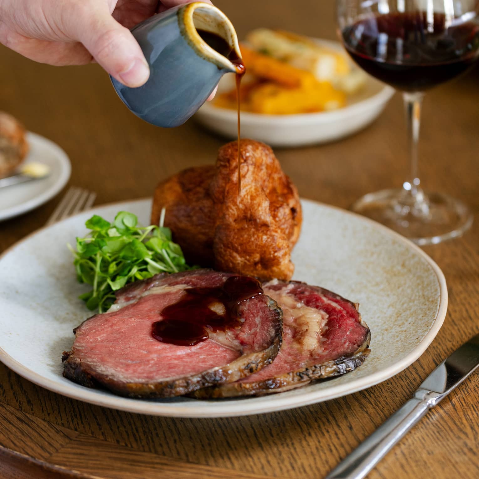 Roast beef slices with Yorkshire pudding and greens garnish with gravy being poured over