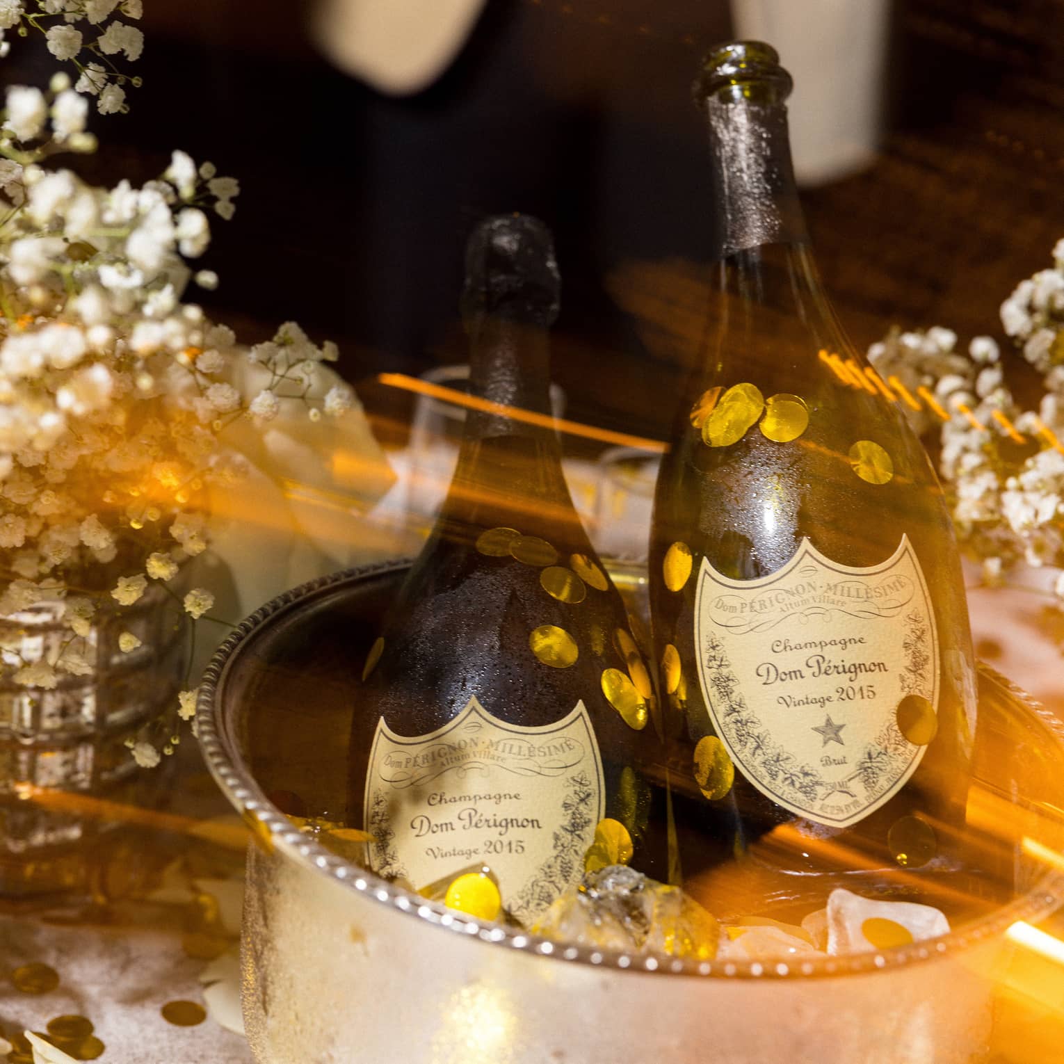 Two bottle of Dom Perignon sit an a silver ice bucket surrounded by white flowers