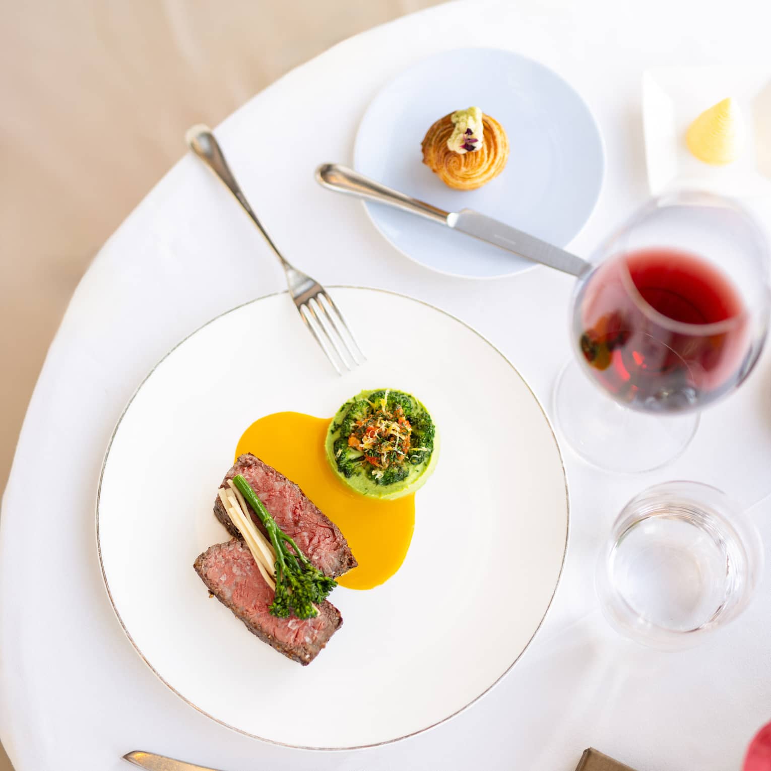 Sliced filet of steak served on a white plate with an orange-coloured sauce and a green vegetable side dish