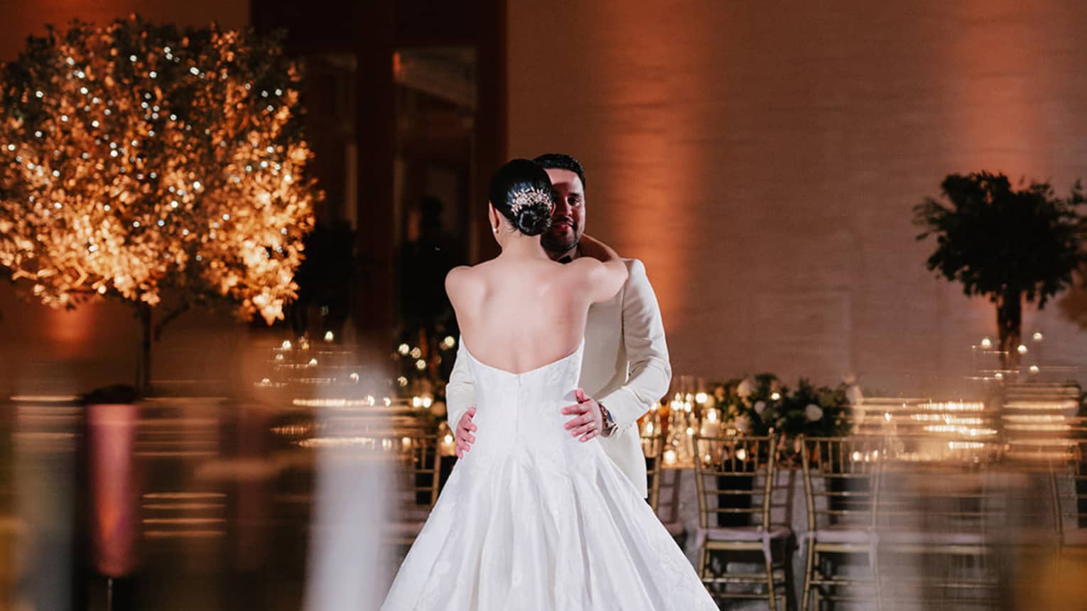 Bride and groom, both wearing white, dance in the centre of a ballroom dance floor