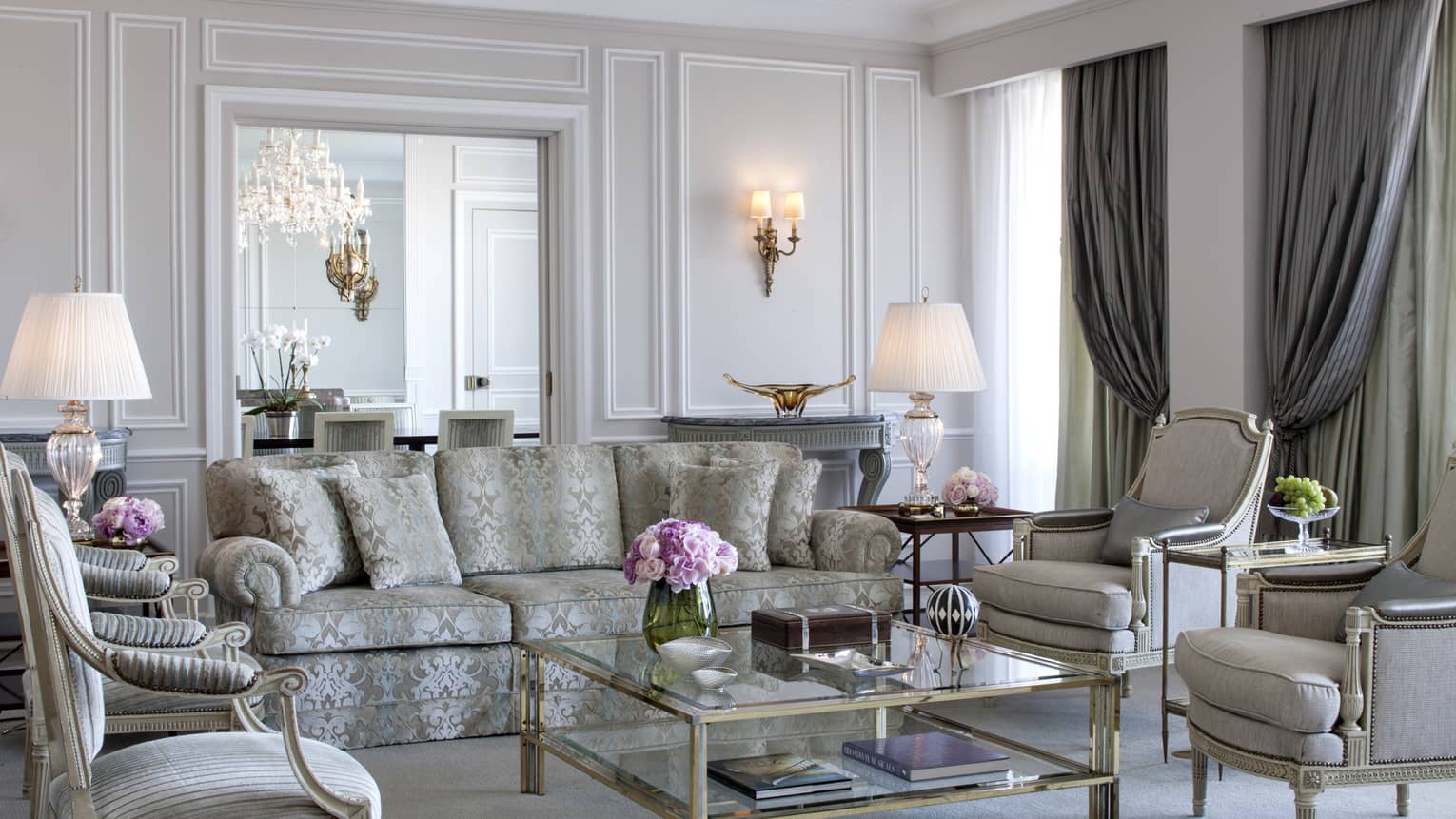 Royal Suite bright, elegant living room with blue-and-grey satin sofa, armchairs, glass coffee table with gold trim, white walls