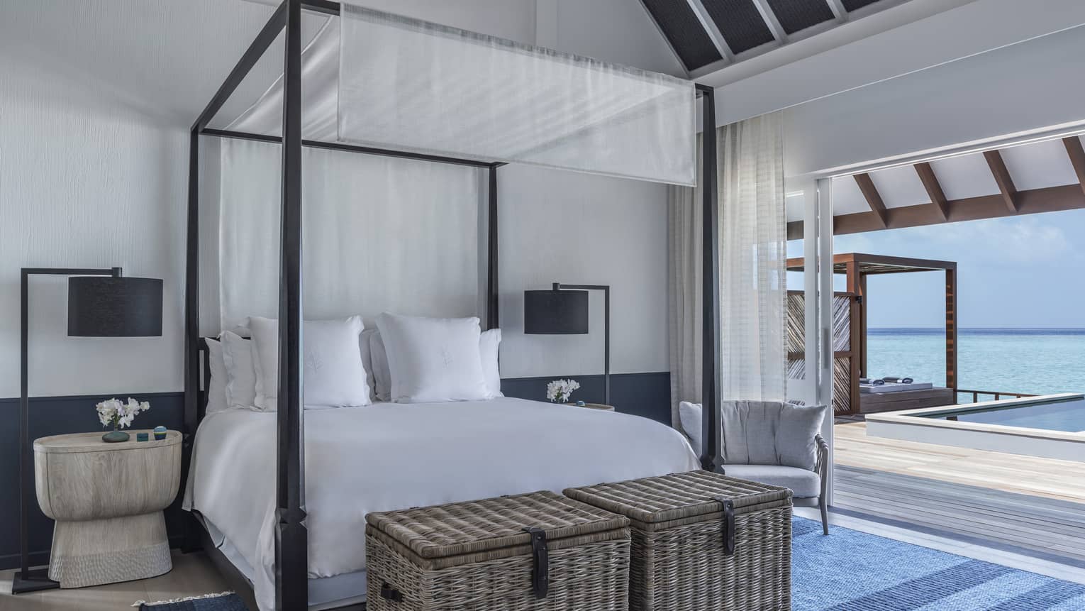 A four poster bed near a sliding door leading to an oceanside pool