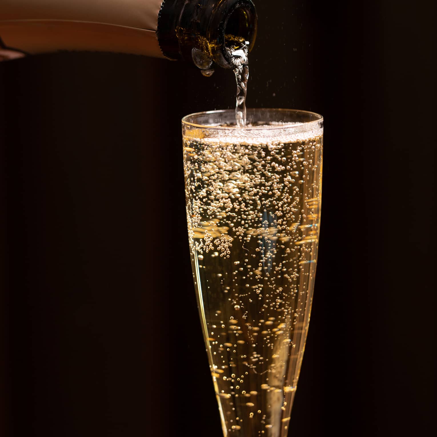 A bottle of champagne is poured into a glass as bubbles float to the top
