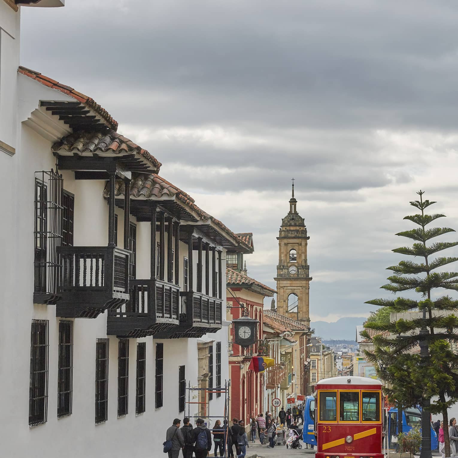 A long view of a busy street on an overcast day, an old clock tower stands out amongst the old buildings lining the street.