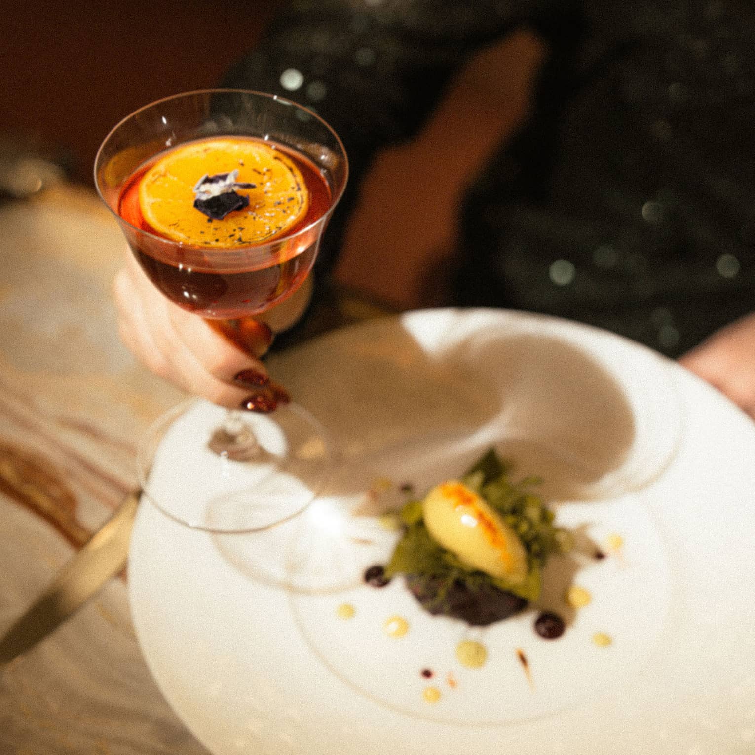 Person holds cocktail glass in hand over a white plate of food