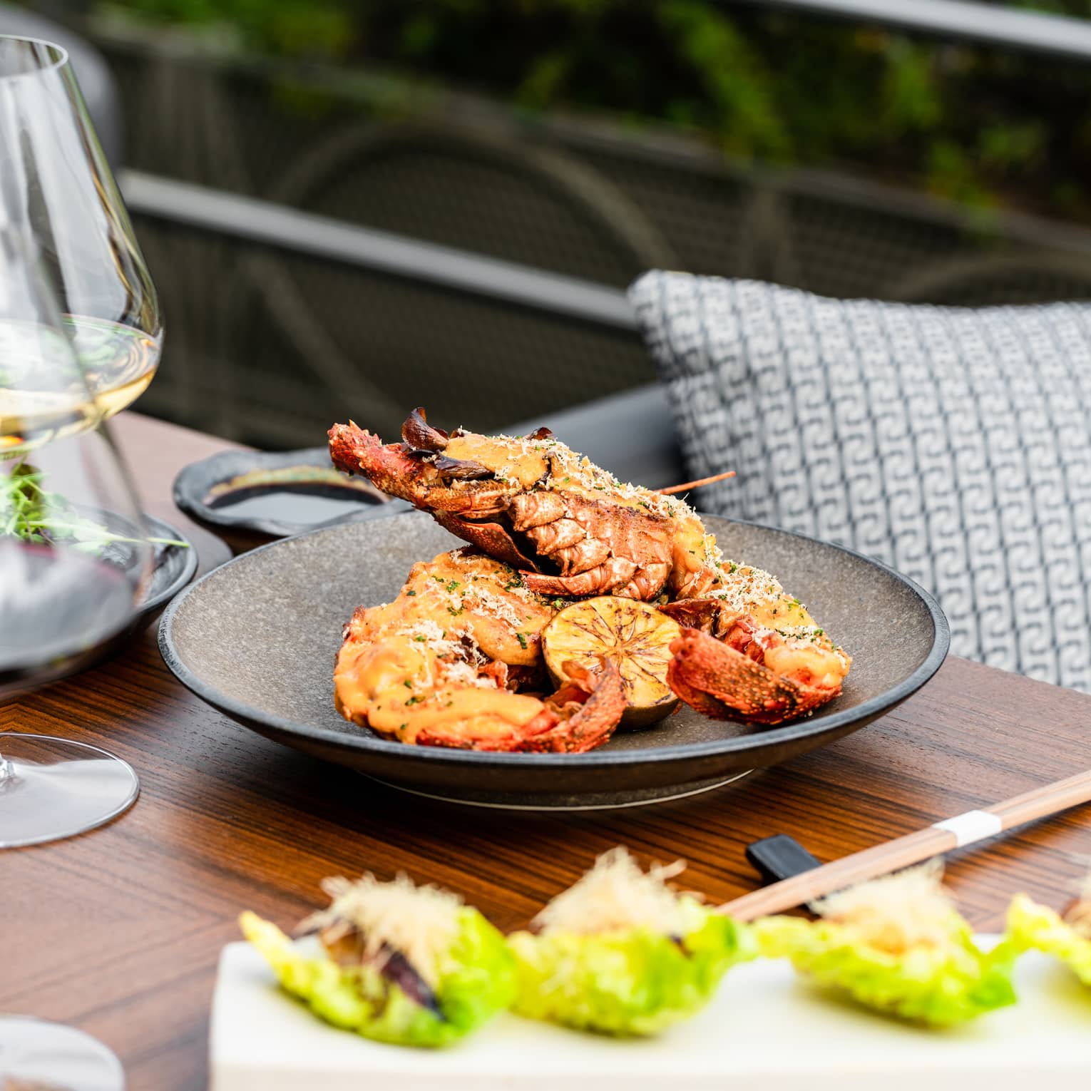 Spiny Lobster Thermidor on brown ceramic dish set on a wooden table with chopsticks
