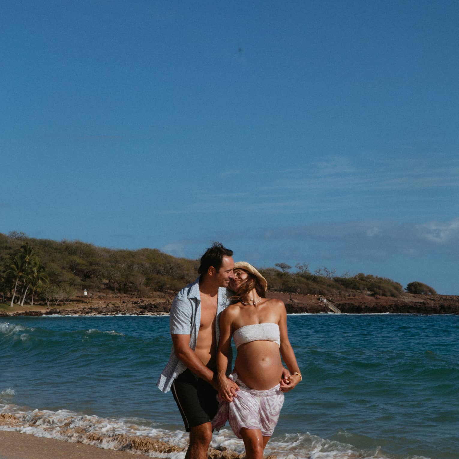 Man and pregnant woman walk together and embrace on the beach
