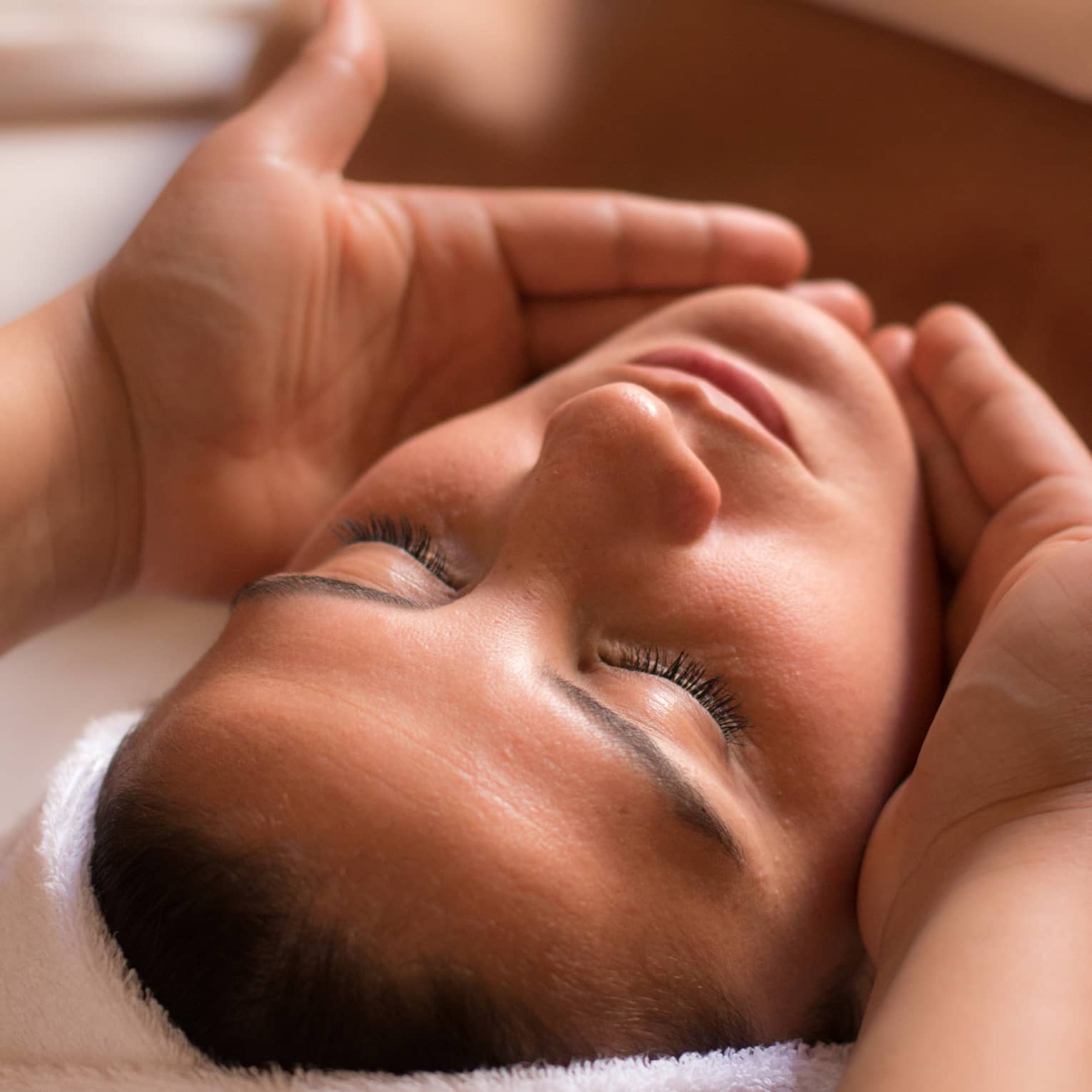 Close-up of woman with eyes closed facing up as hands cup her face and chin