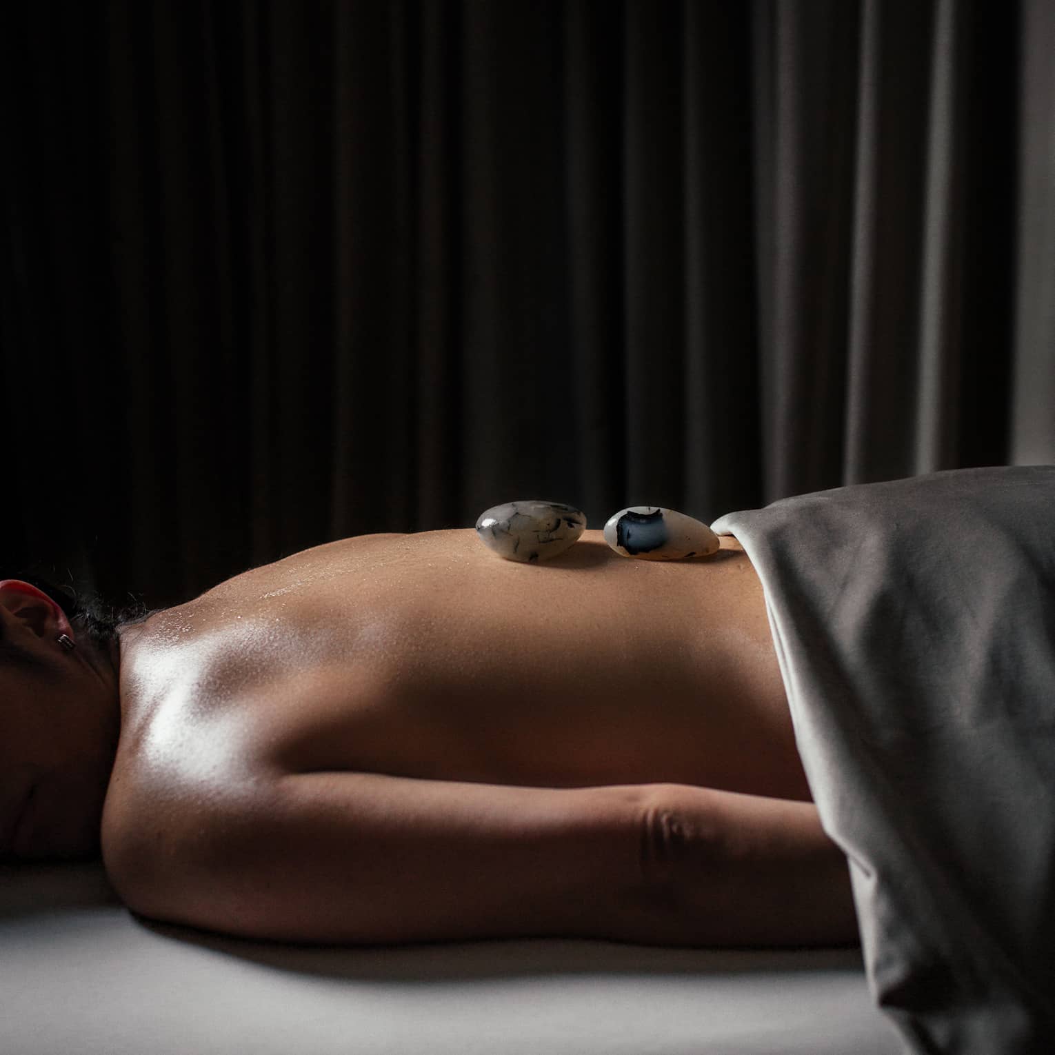 A woman with small stones on her back in a spa treatment room.