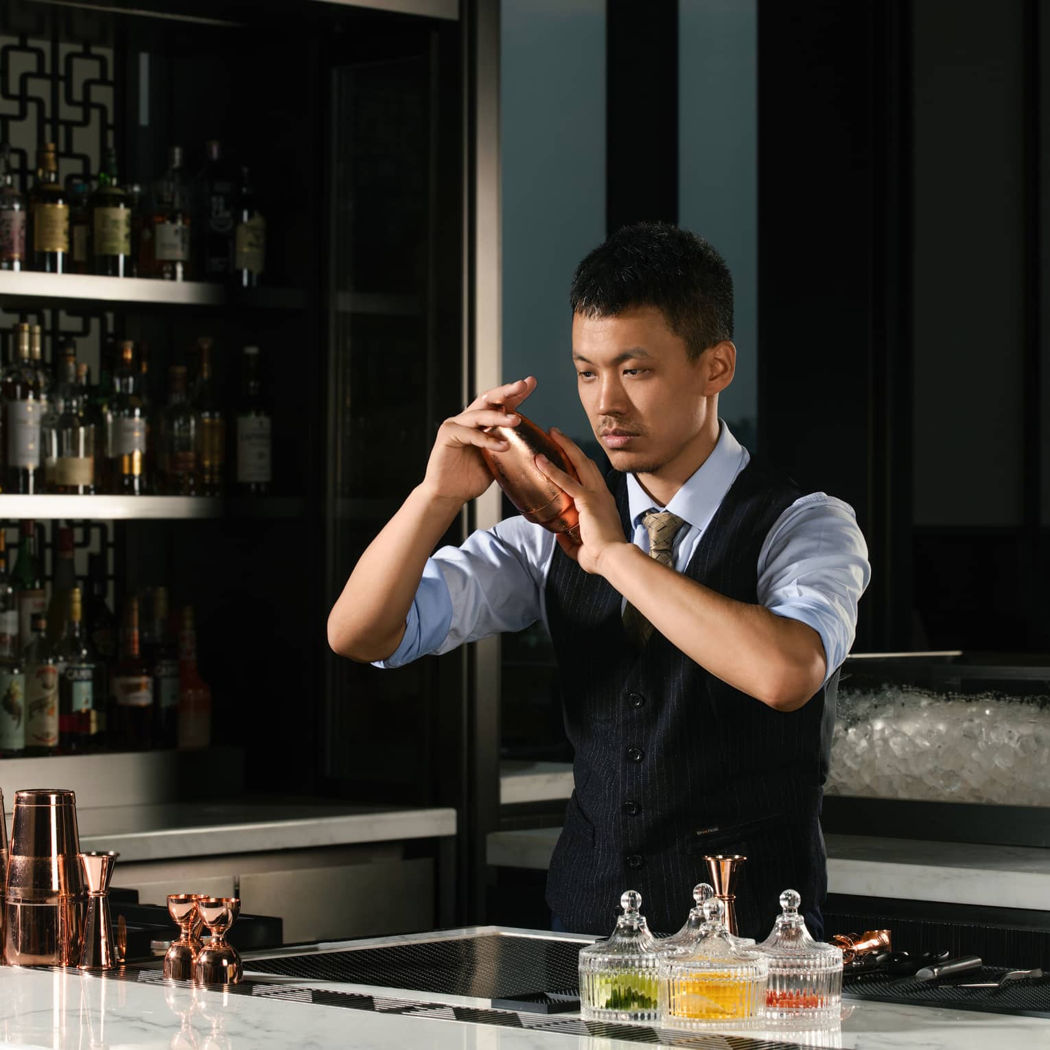 William Zhang, bartender, behind the counter shaking a cocktail