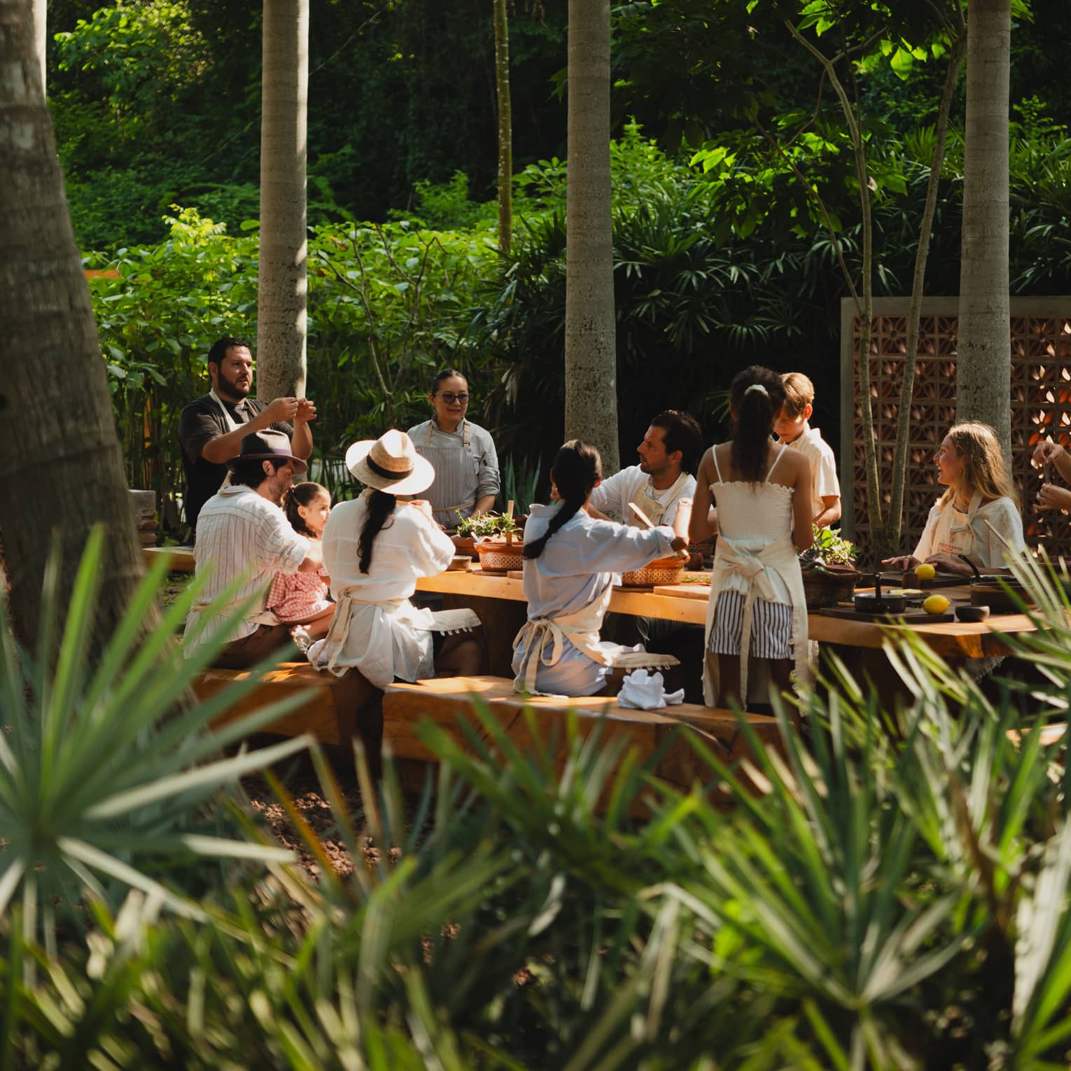 People seated around a long outdoor dining table set among palm trees