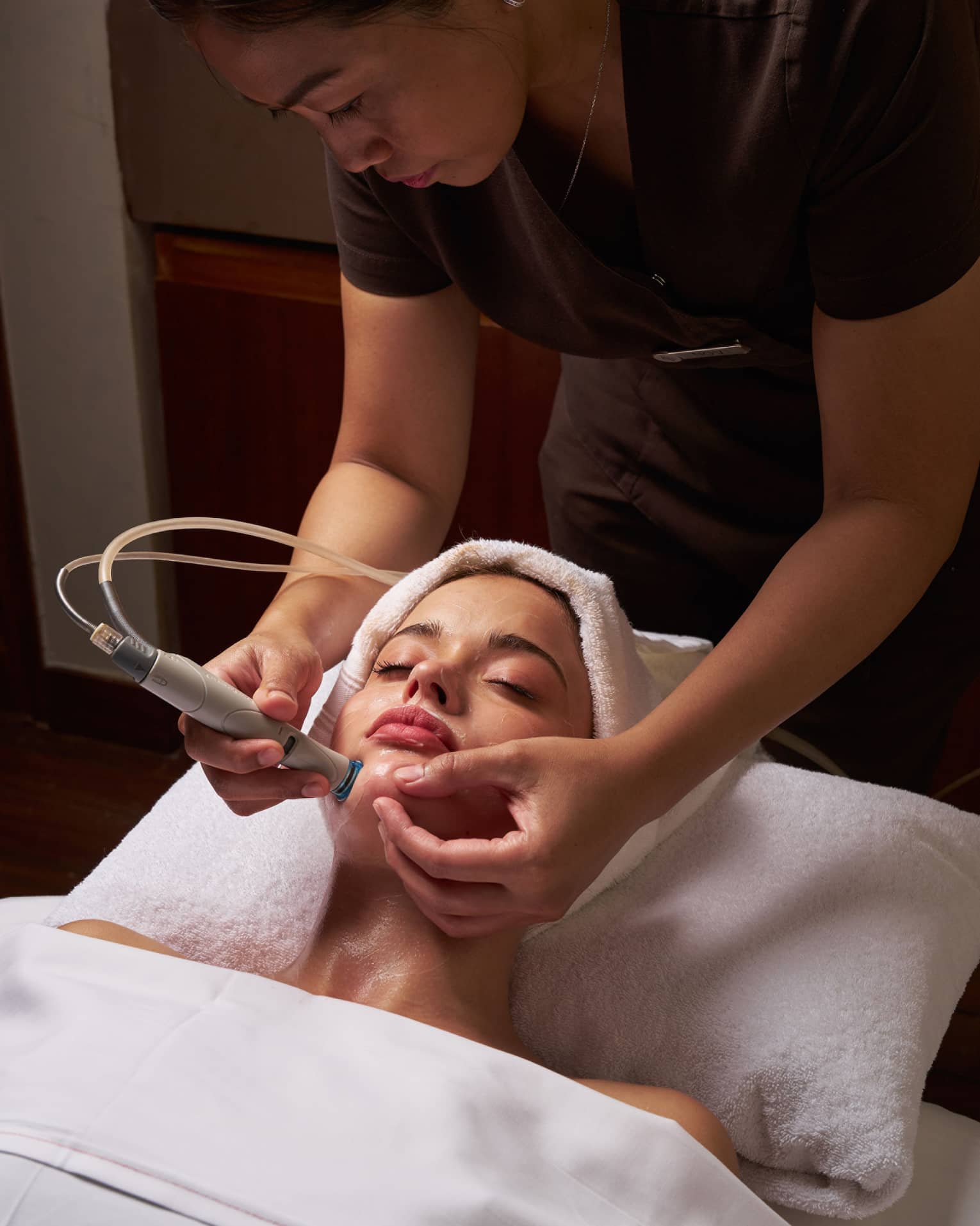 Spa therapist performs facial on female guest with tool