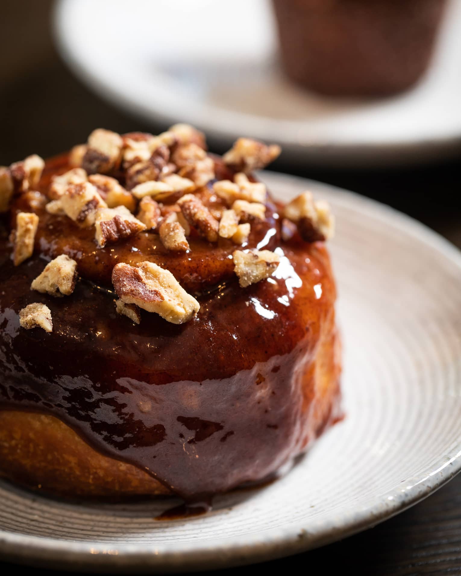 A brown pastry with nuts on it resting on a small white plate.